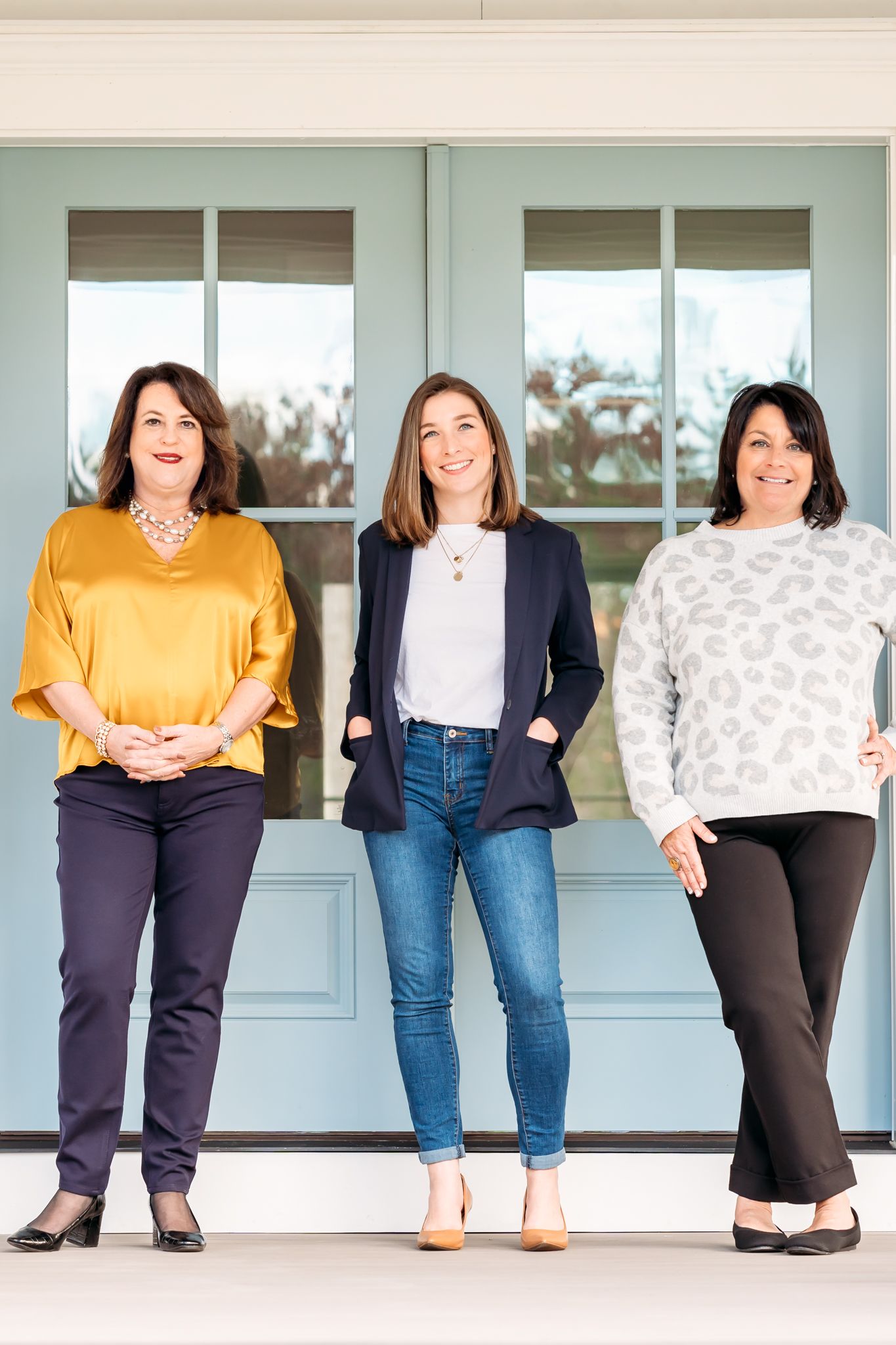 A group of women in business attire stand together against a light blue wall, showing only their torsos and legs.