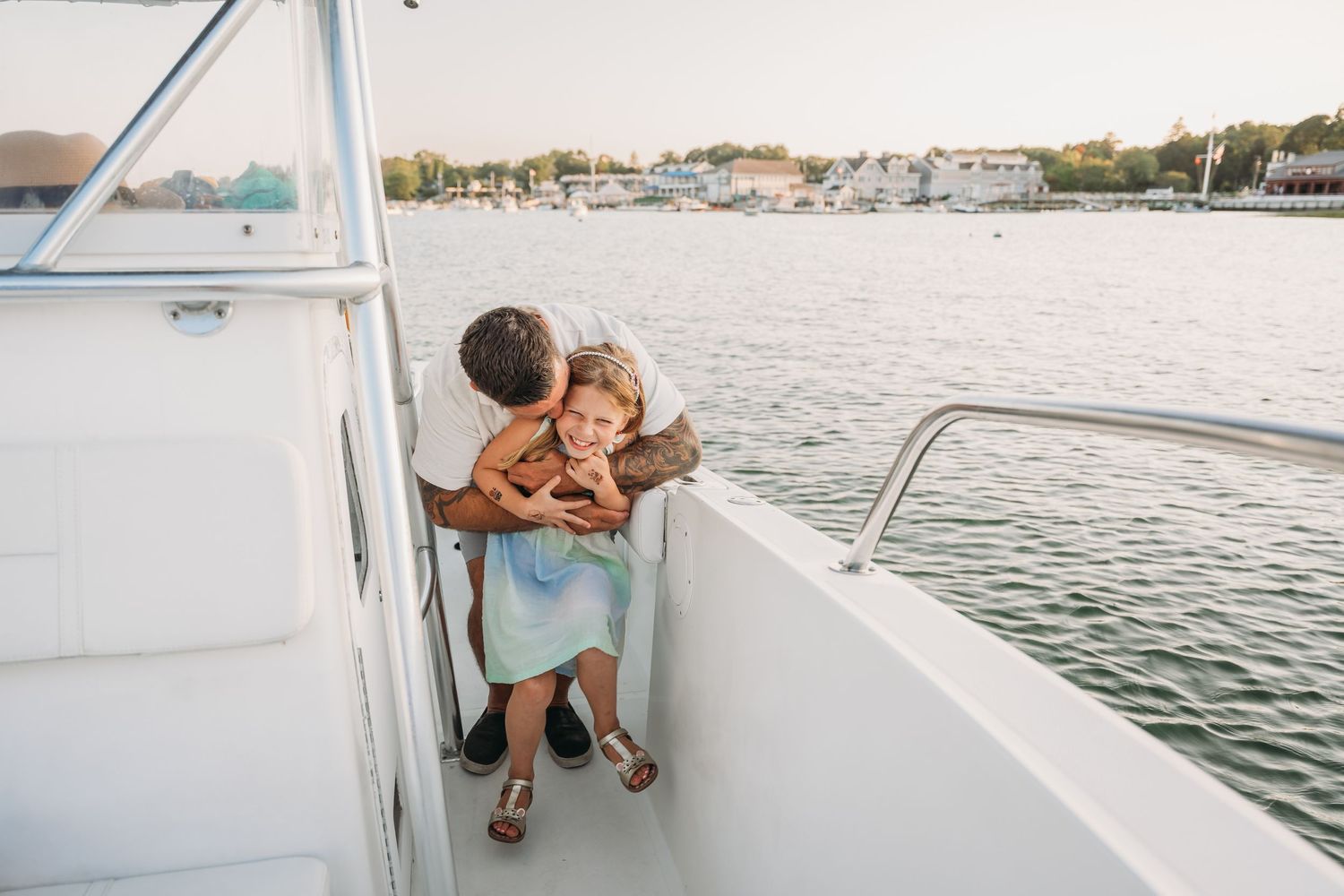 Two people share a tender embrace while standing on a boat deck overlooking a marina at sunset.