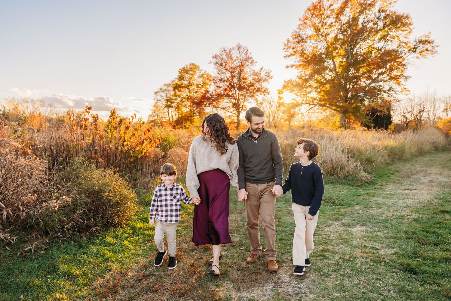 A family walking together on a grassy path at sunset during golden hour with warm autumn lighting.