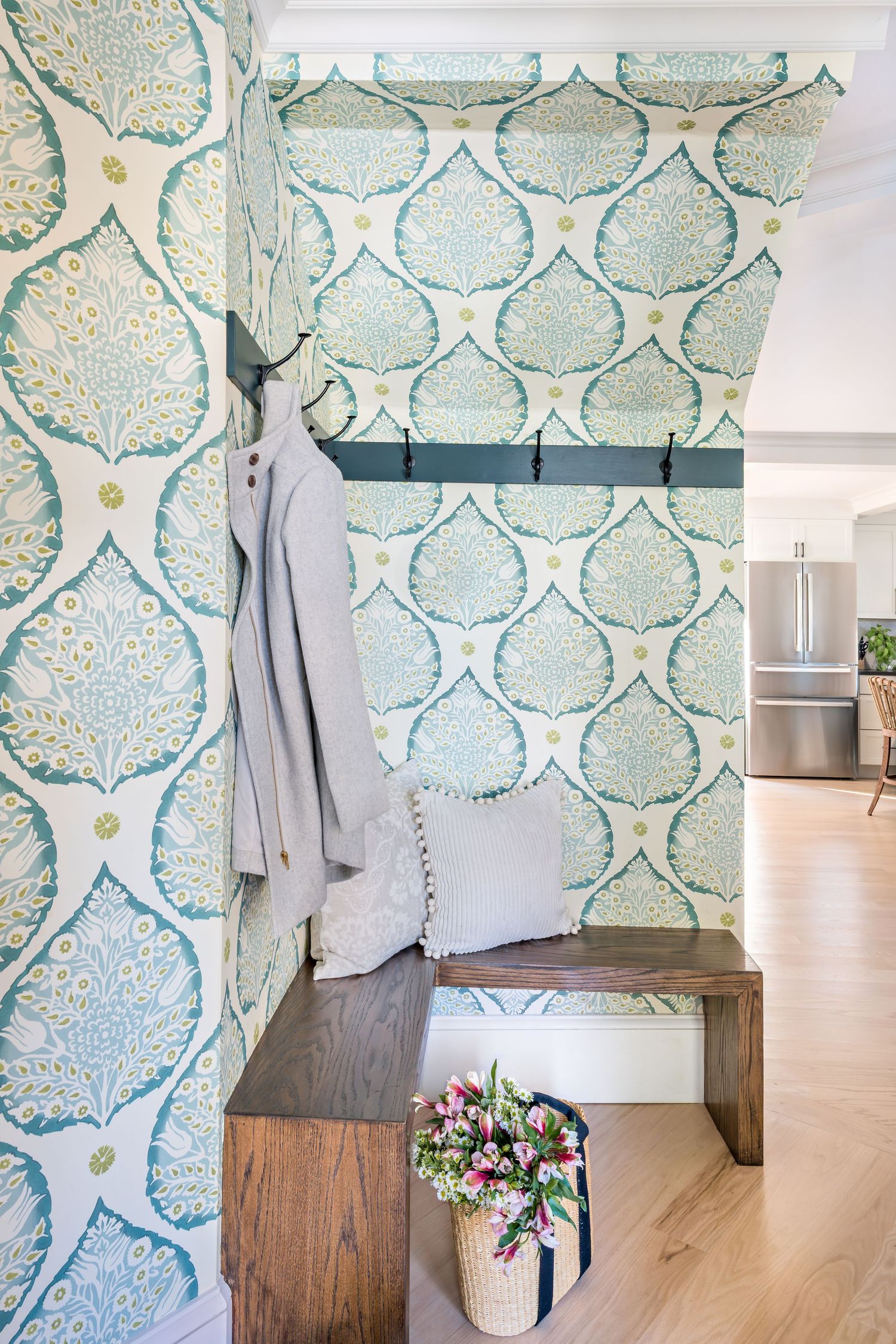 Modern room interior with turquoise damask wallpaper, wooden bench, and hanging gray coat against patterned wall.