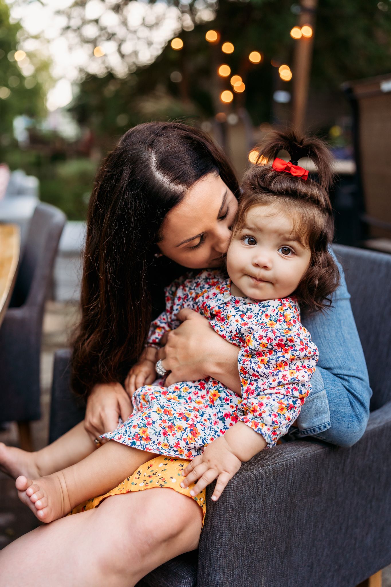A tender moment shared between parent and child sitting on a couch outdoors with string lights in the background.