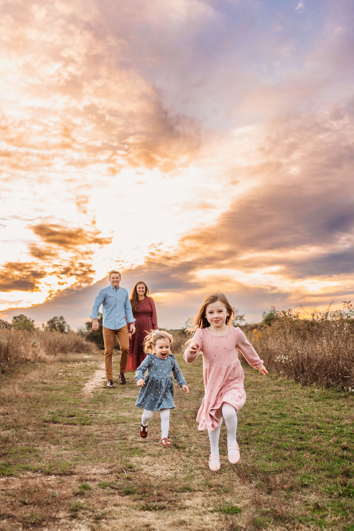 Family running and playing together in a field during golden sunset with dramatic cloudy sky.