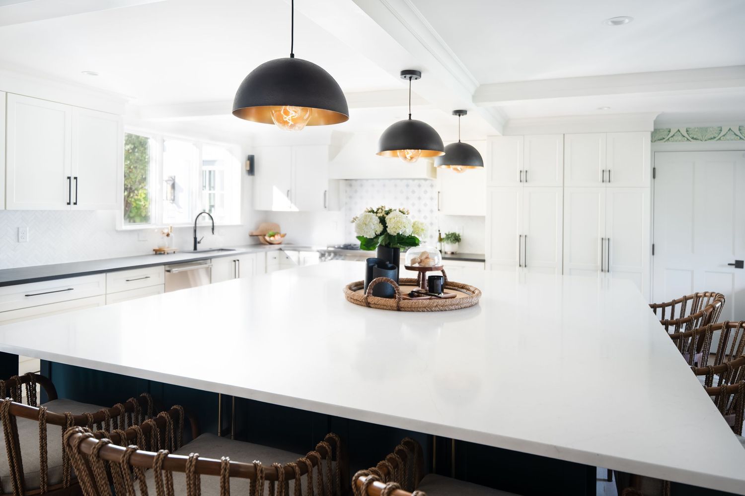 Modern white kitchen with black pendant lights, quartz countertops and wood bar stools features clean lines and open design.