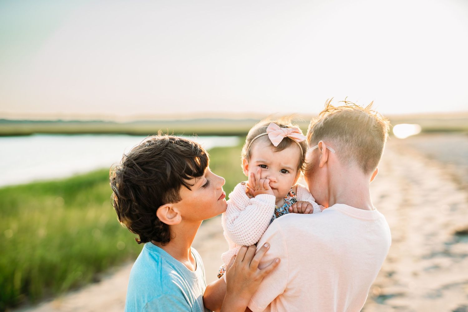 A family shares a tender moment together on a sunny path by the water during golden hour.