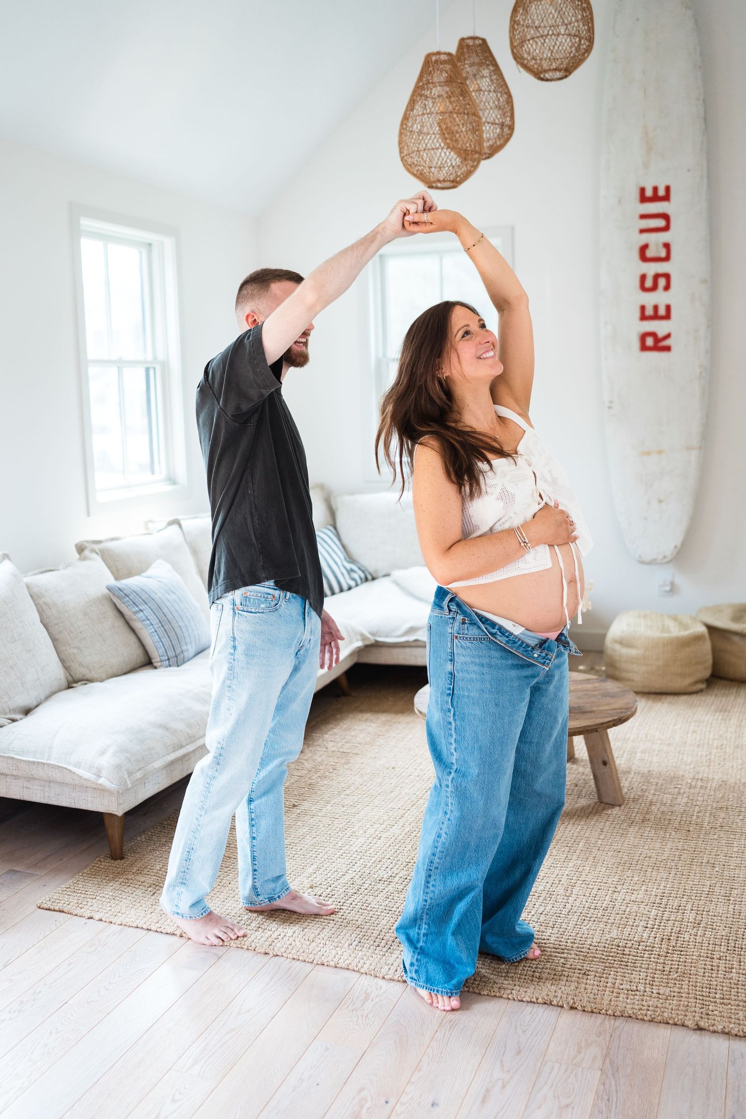 A couple dancing together in a bright white room with rattan pendant lights and a beige rug.
