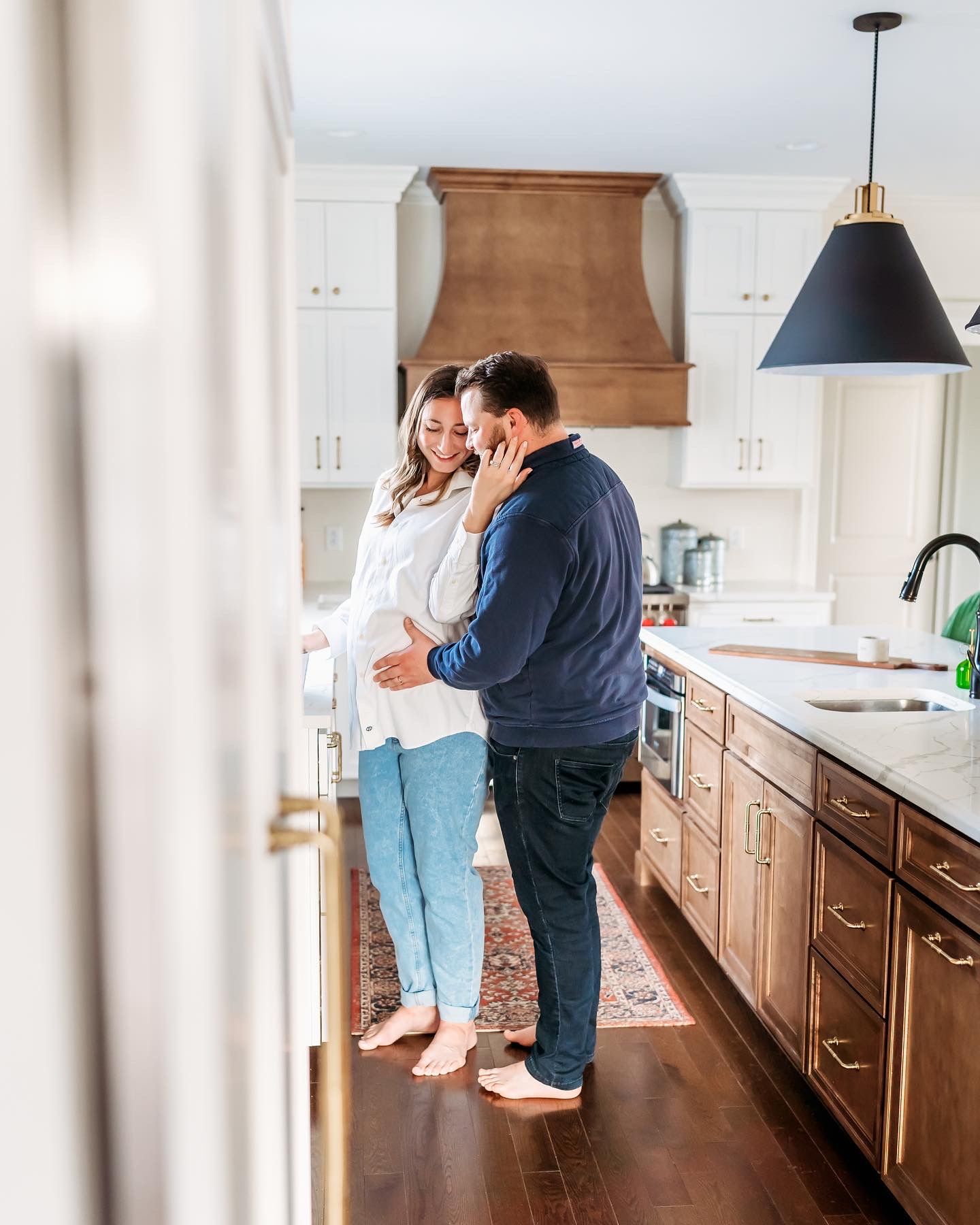 A couple embraces in their modern kitchen with white cabinets and wooden floors while sharing an intimate moment.