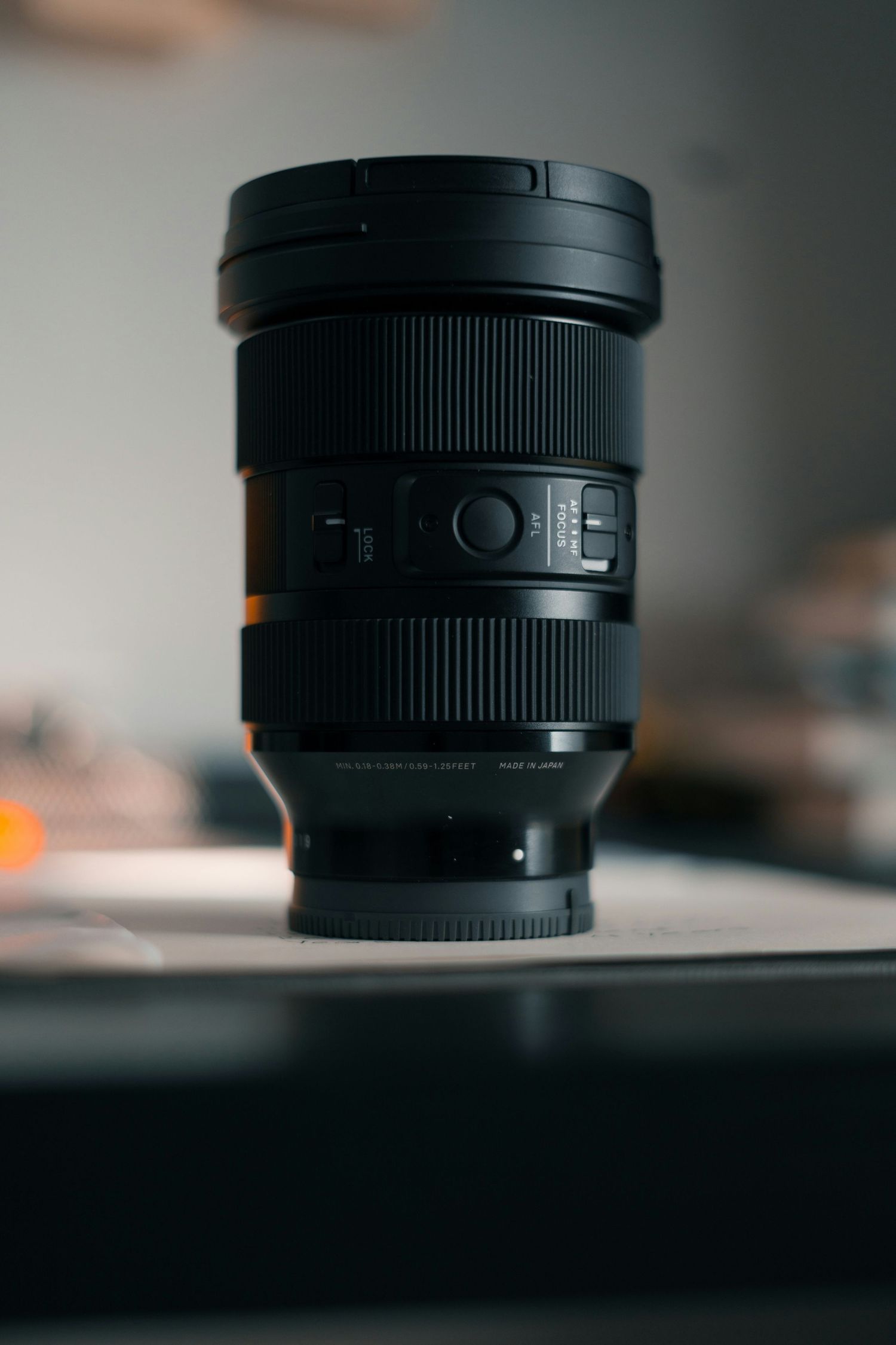A professional black camera lens with ribbed texture and control switches sits on a dark surface in moody lighting.