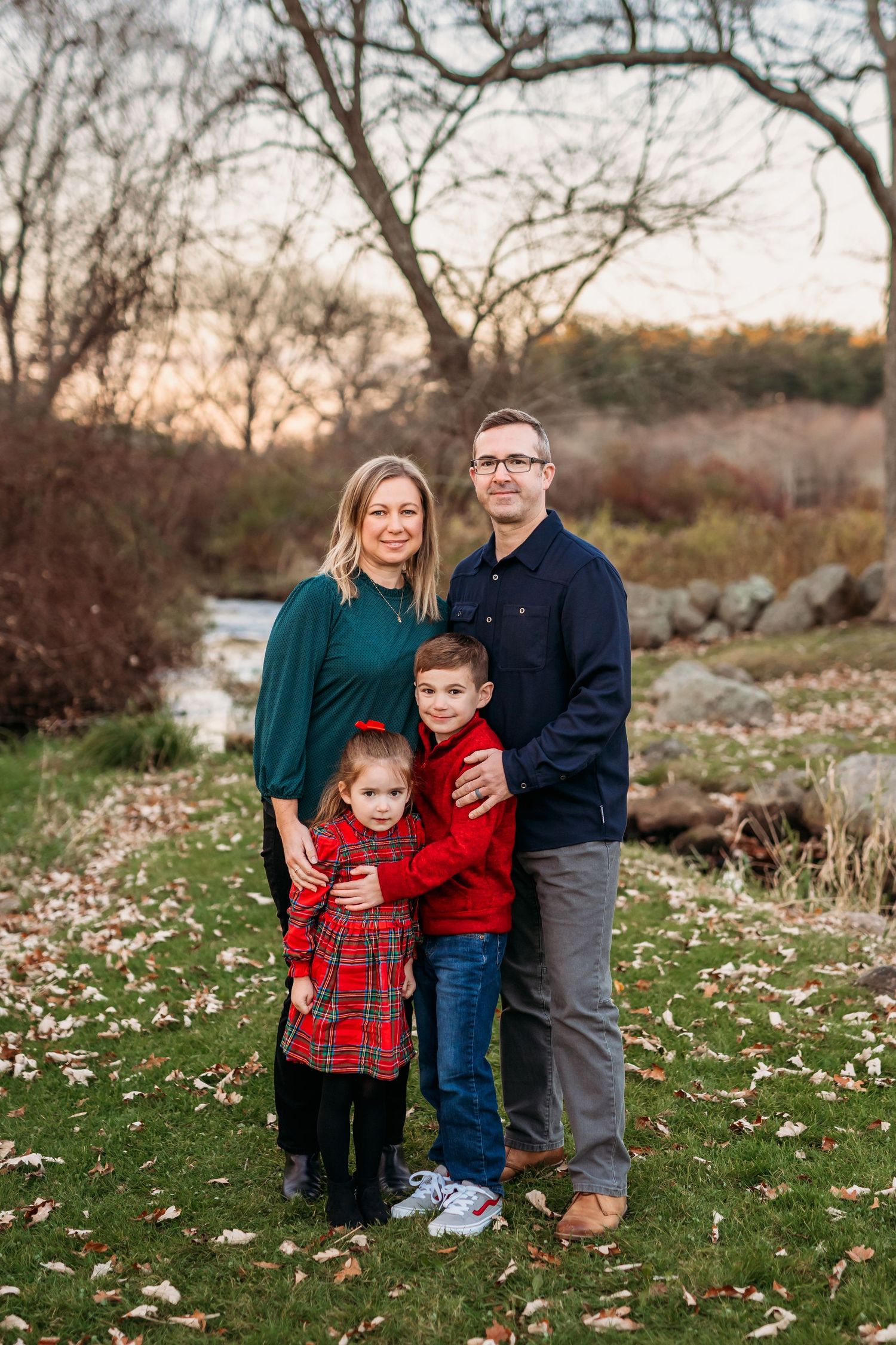 A family in coordinating green and plaid outfits poses together on grass during an autumn sunset photoshoot.