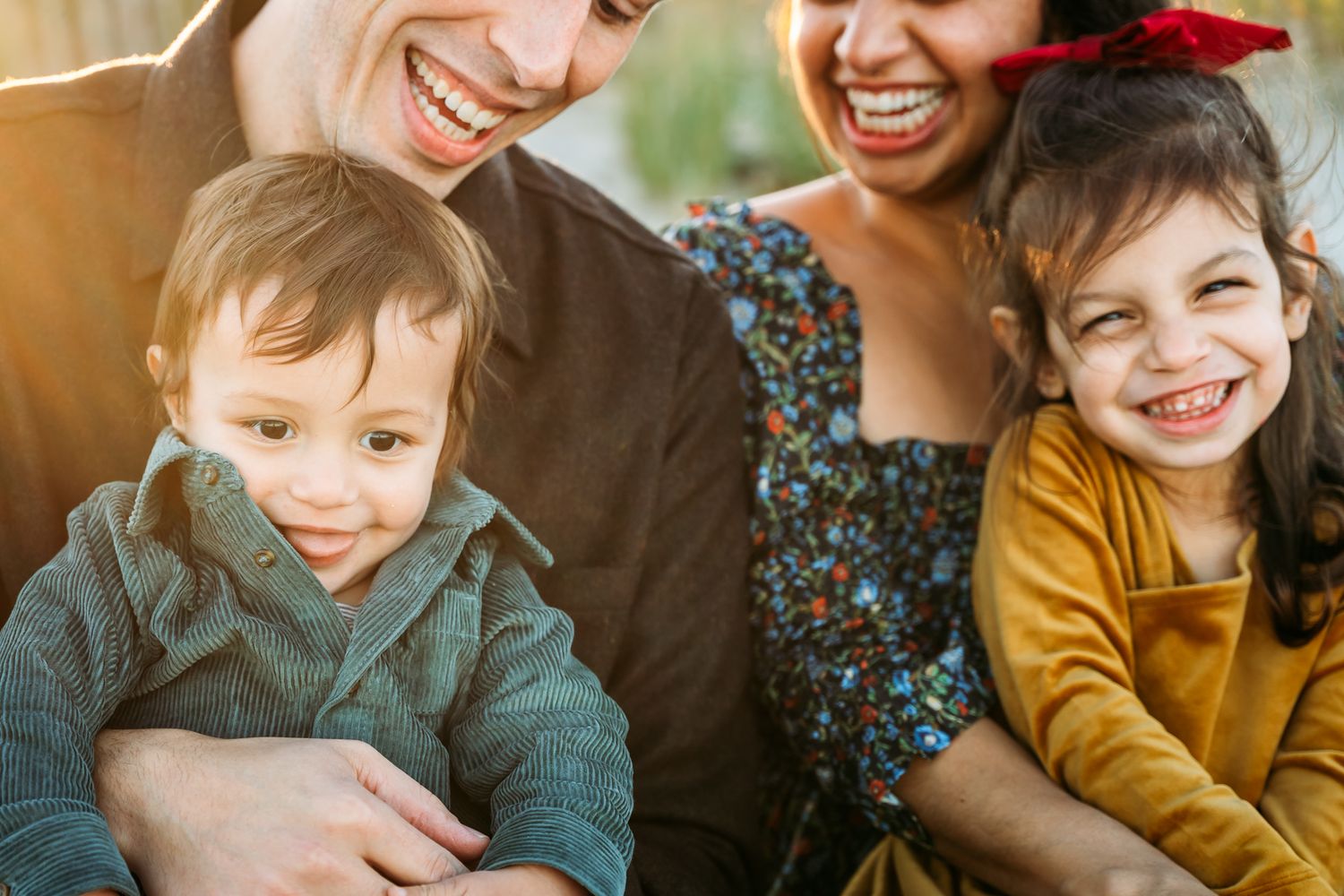 Two happy mothers laughing with their young children in warm sunlight, enjoying a joyful family moment together.