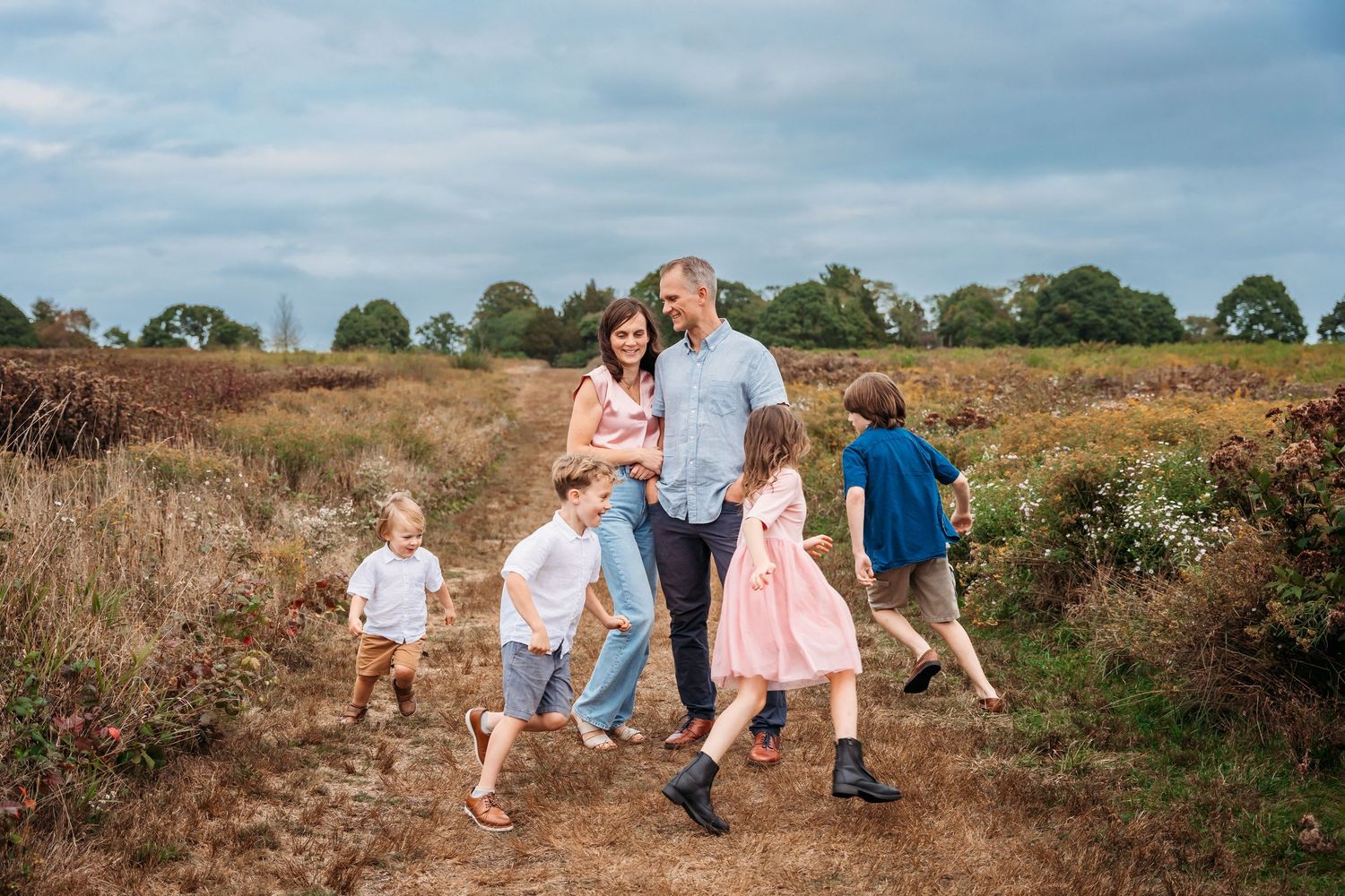 A series of candid outdoor family photos showing people walking and playing together in a rustic field setting at sunset.
