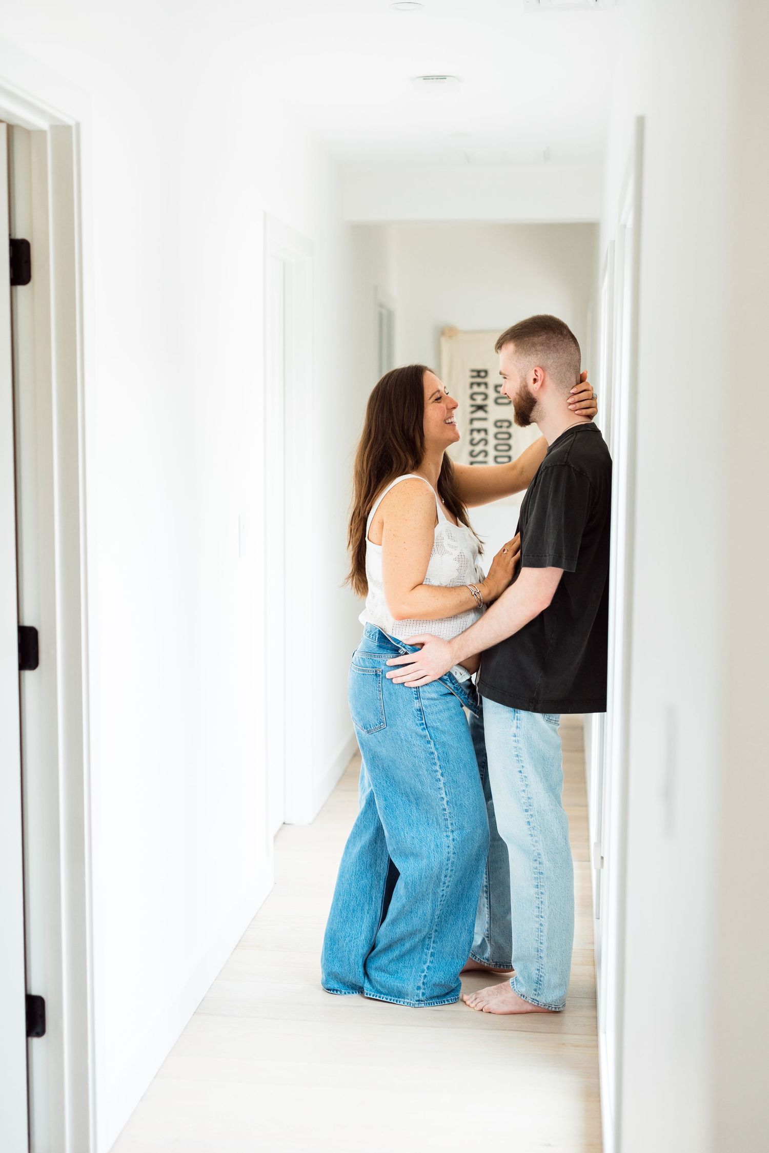 Couple in casual clothing embraces and kisses in bright white hallway with mirrored reflections.