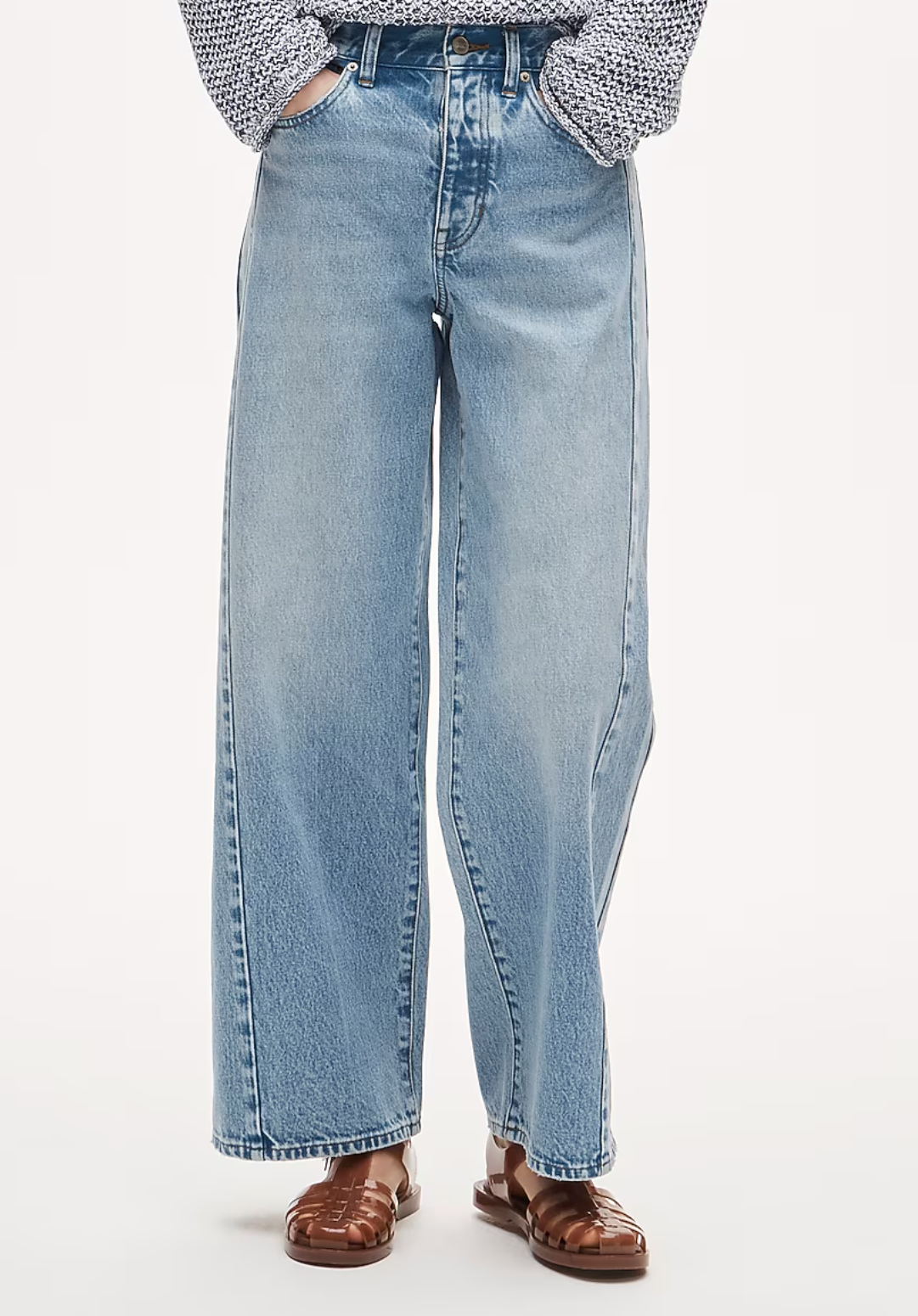 Wide-leg light wash blue jeans with a high waist, worn with brown leather sandals and a patterned top.