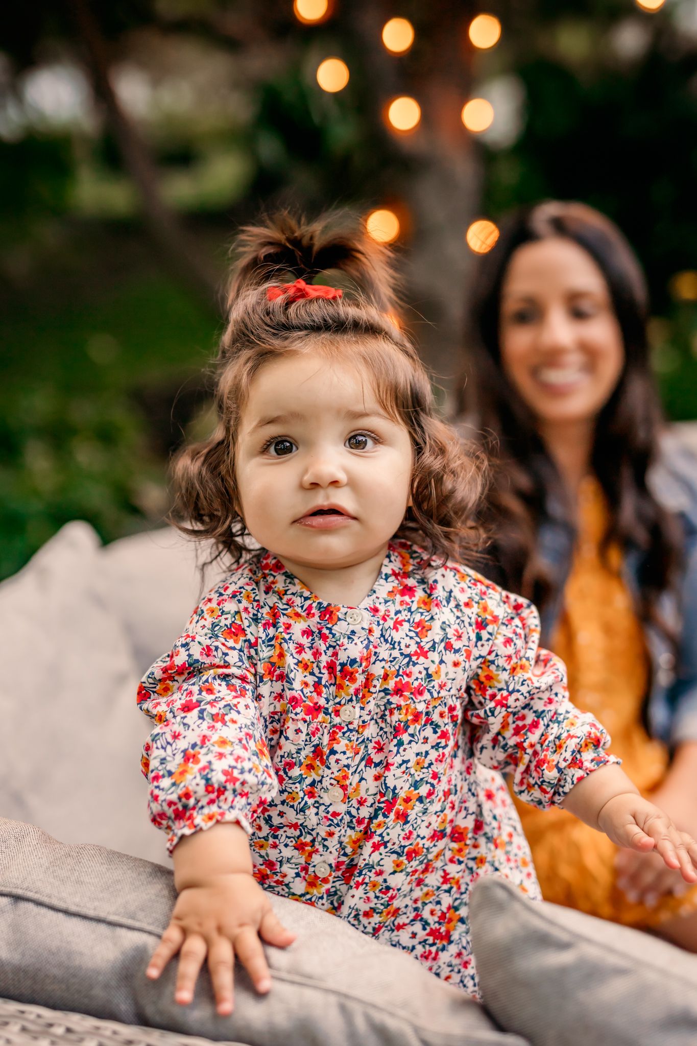 Baby in floral dress crawls on concrete surface with bokeh lights in background.