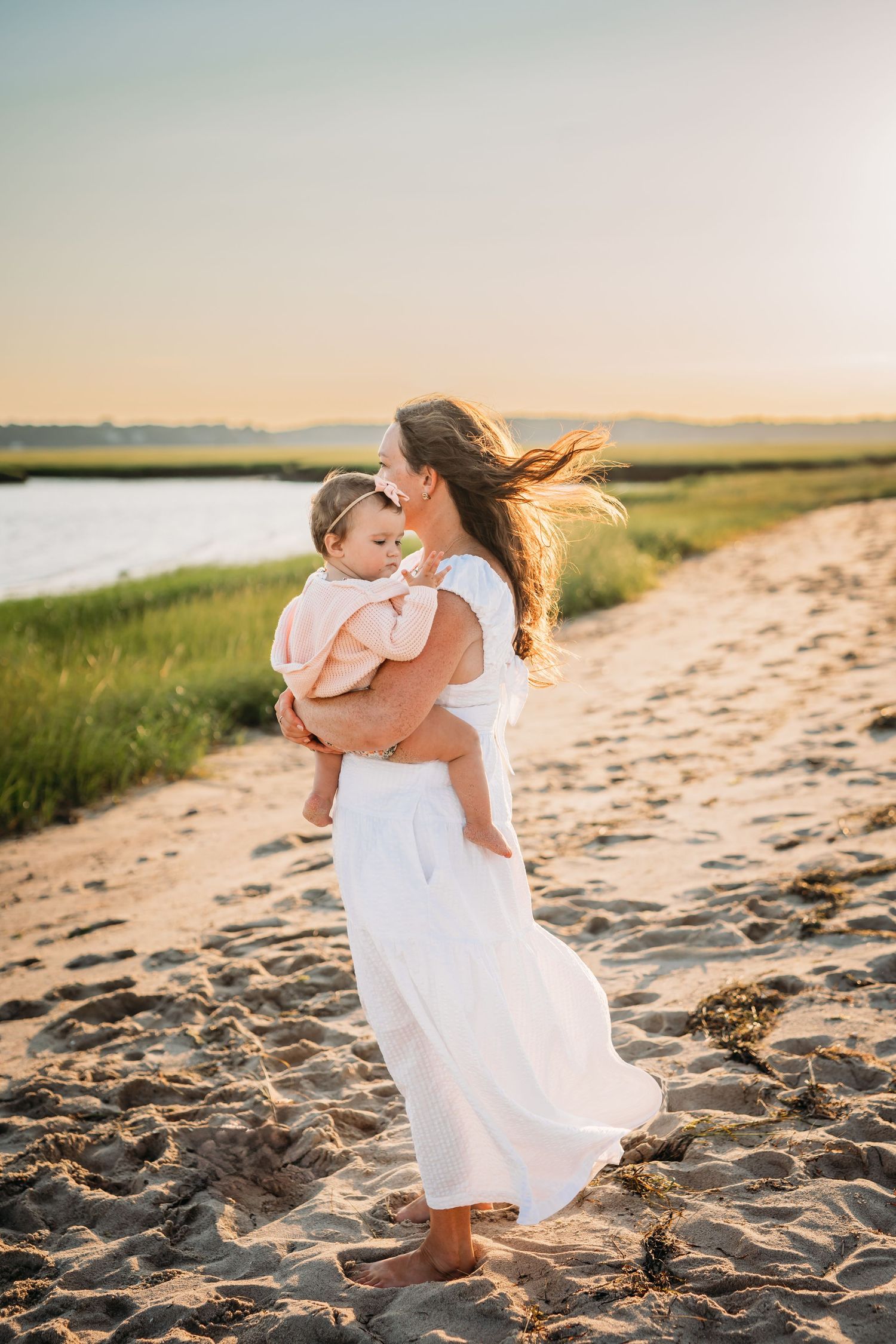 A tender embrace between two people in white dresses on a sandy beach at sunset.