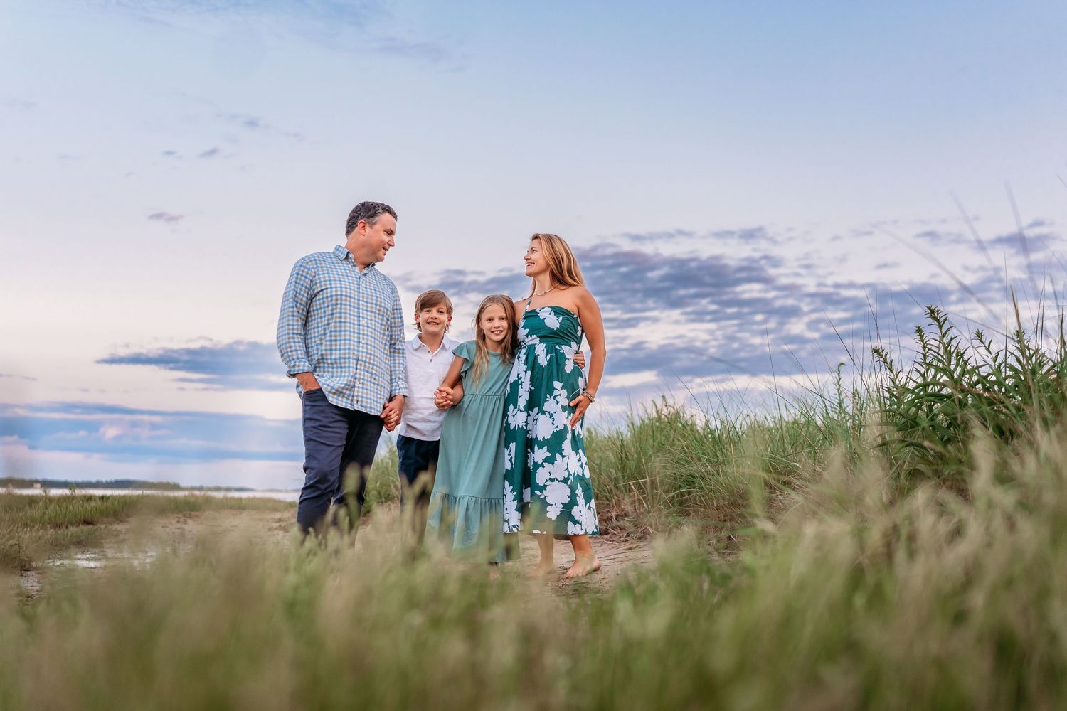 A family of four stands together in tall grass along the coast at sunset.