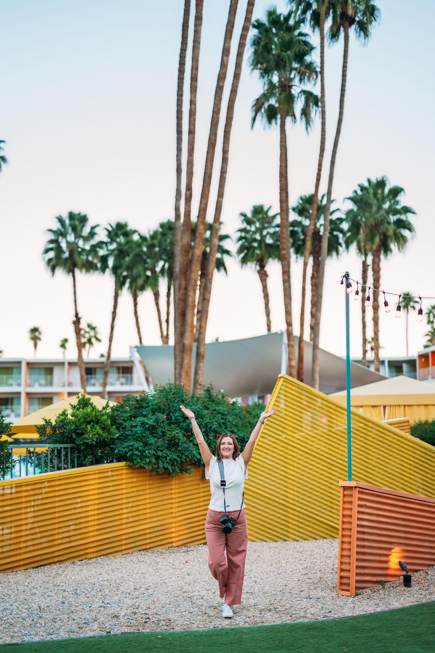 Colorful yellow geometric walls and palm trees create a retro mid-century modern aesthetic at a desert hotel.