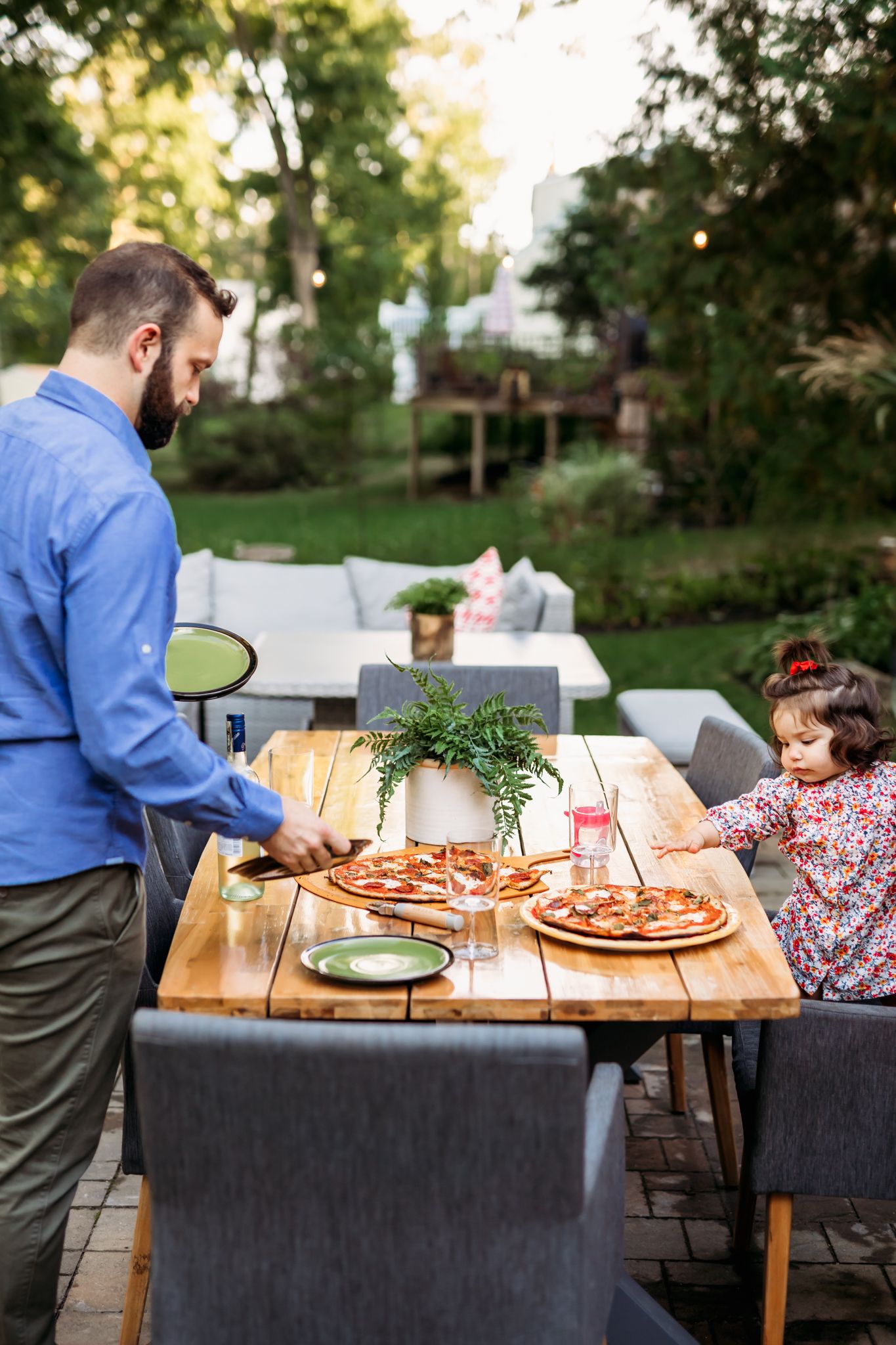People enjoying pizza at an outdoor dining table on a patio with lush greenery in the background.