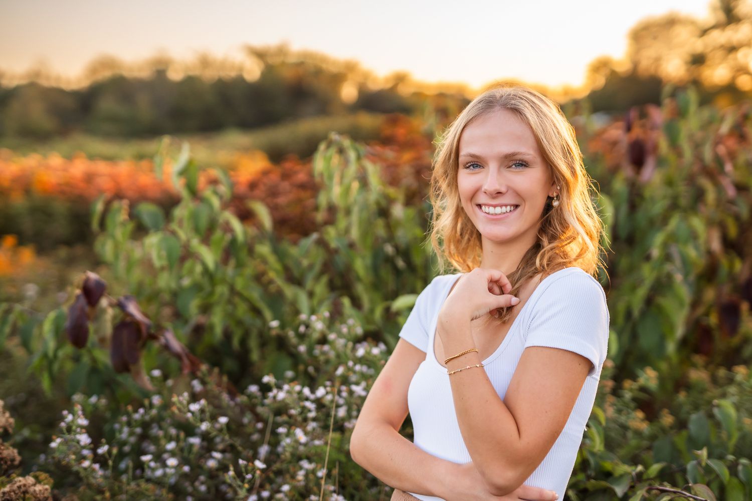 A person in a white dress poses in a garden at sunset with wildflowers and greenery in the background.