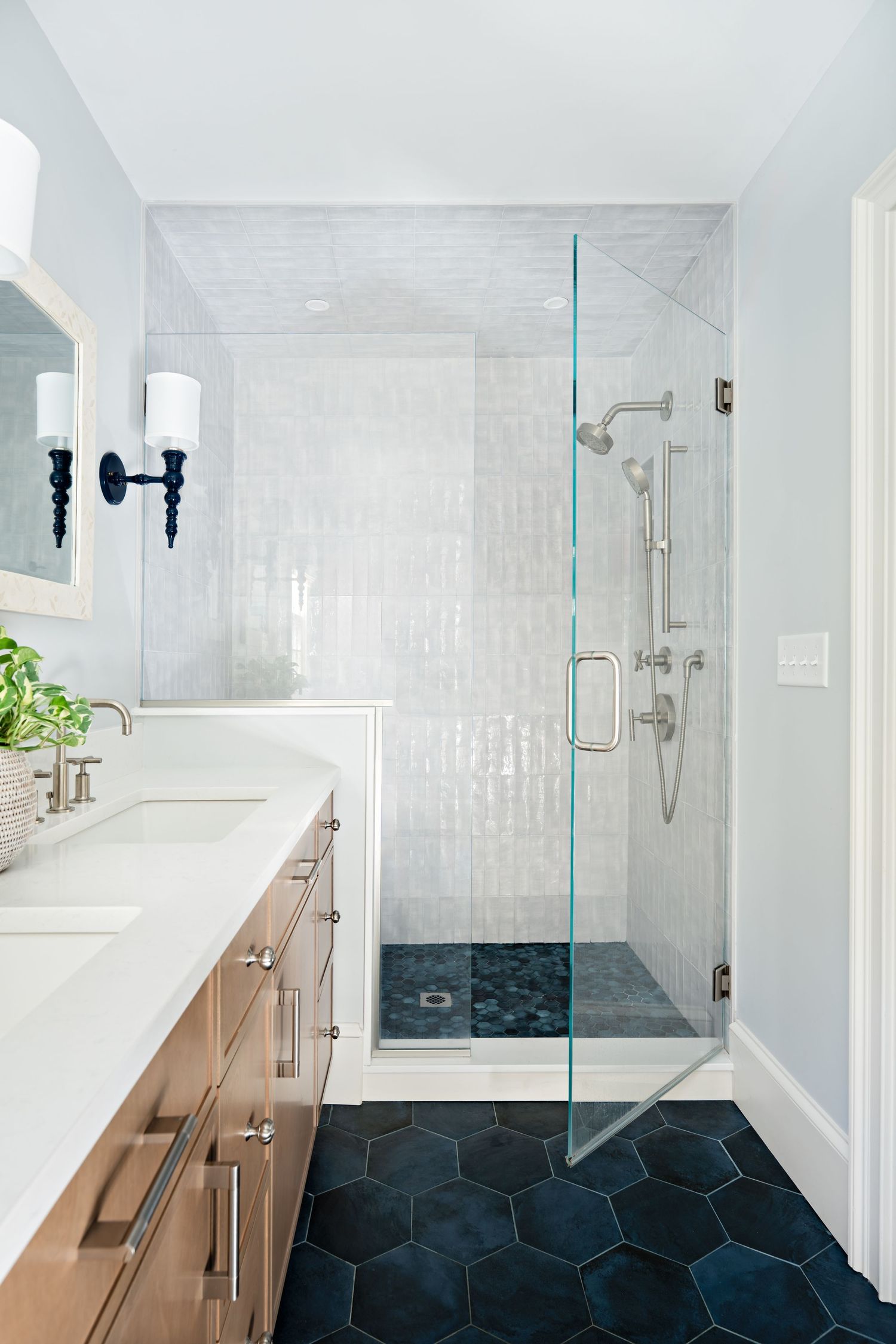 Modern bathroom interior with white walls, wooden vanity, and black hexagonal floor tiles features a glass shower enclosure.