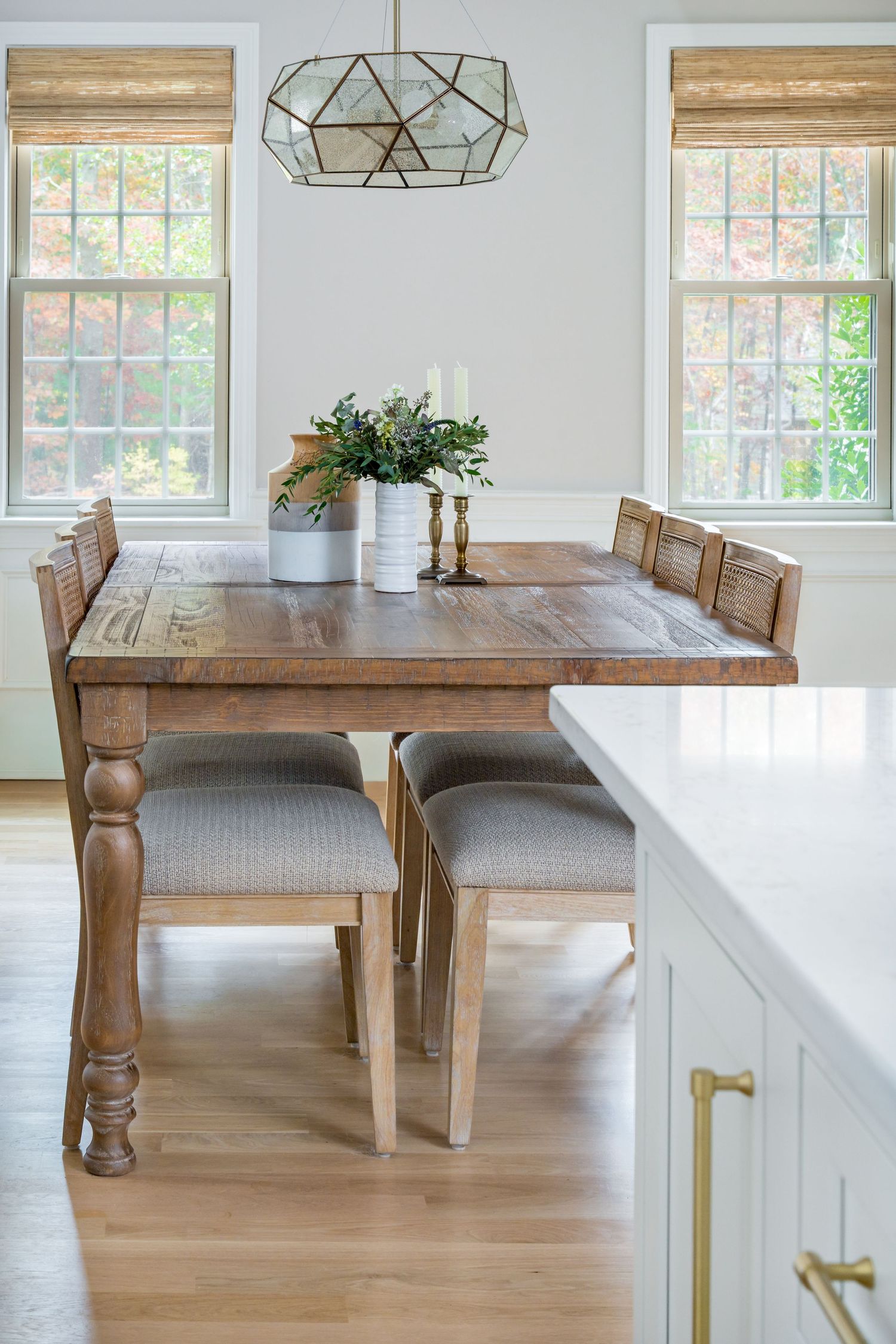 Modern dining room with wooden table, geometric pendant light, bamboo shades, and white walls creates a bright airy space.