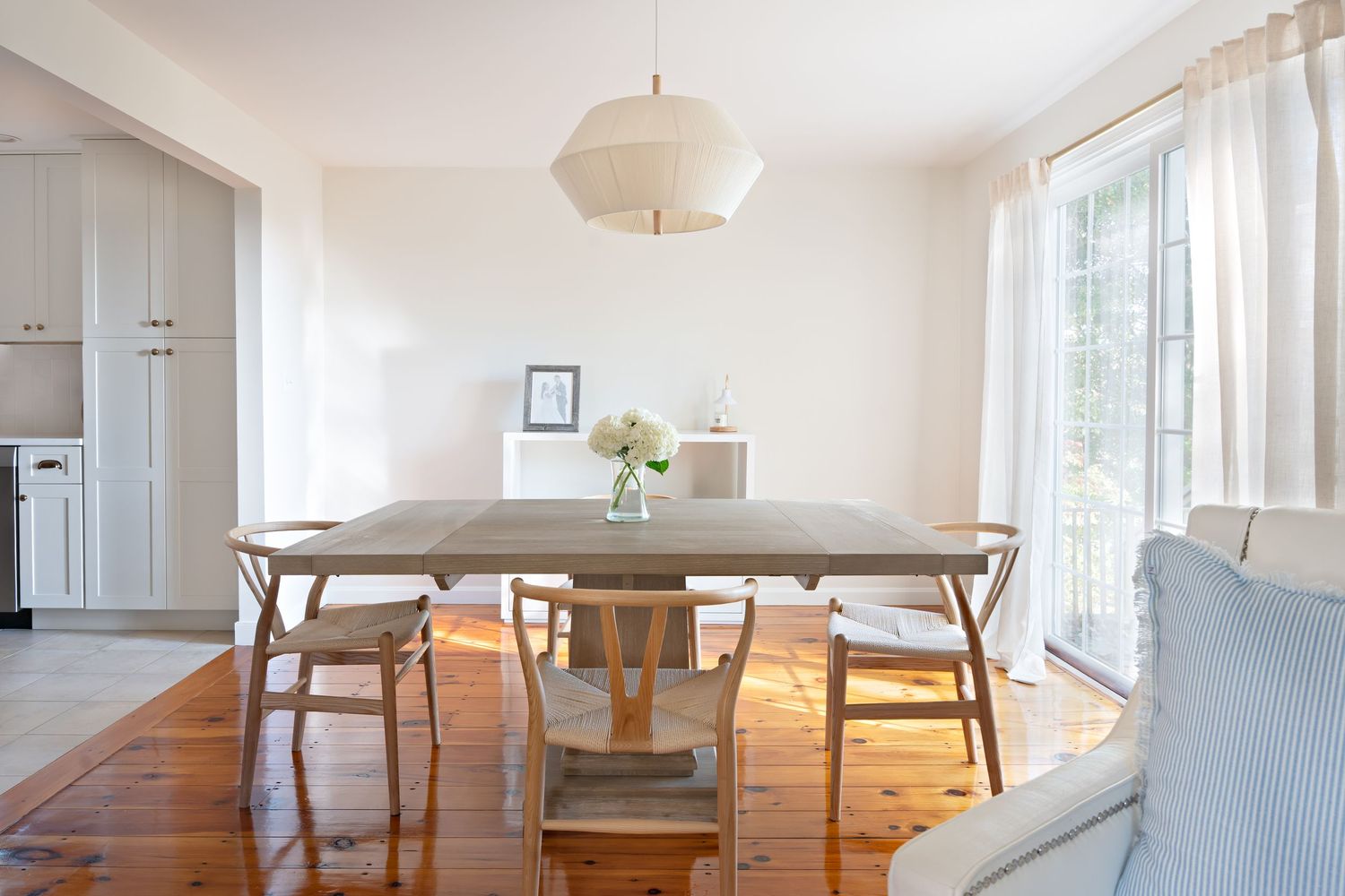 Bright and airy modern dining room with wooden floors, white walls, and round paper lantern pendant light.