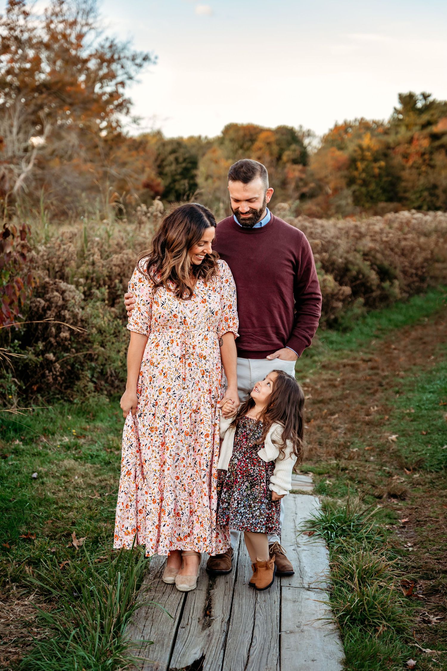 A family stands together on a wooden walkway surrounded by autumn foliage during a fall photo session.