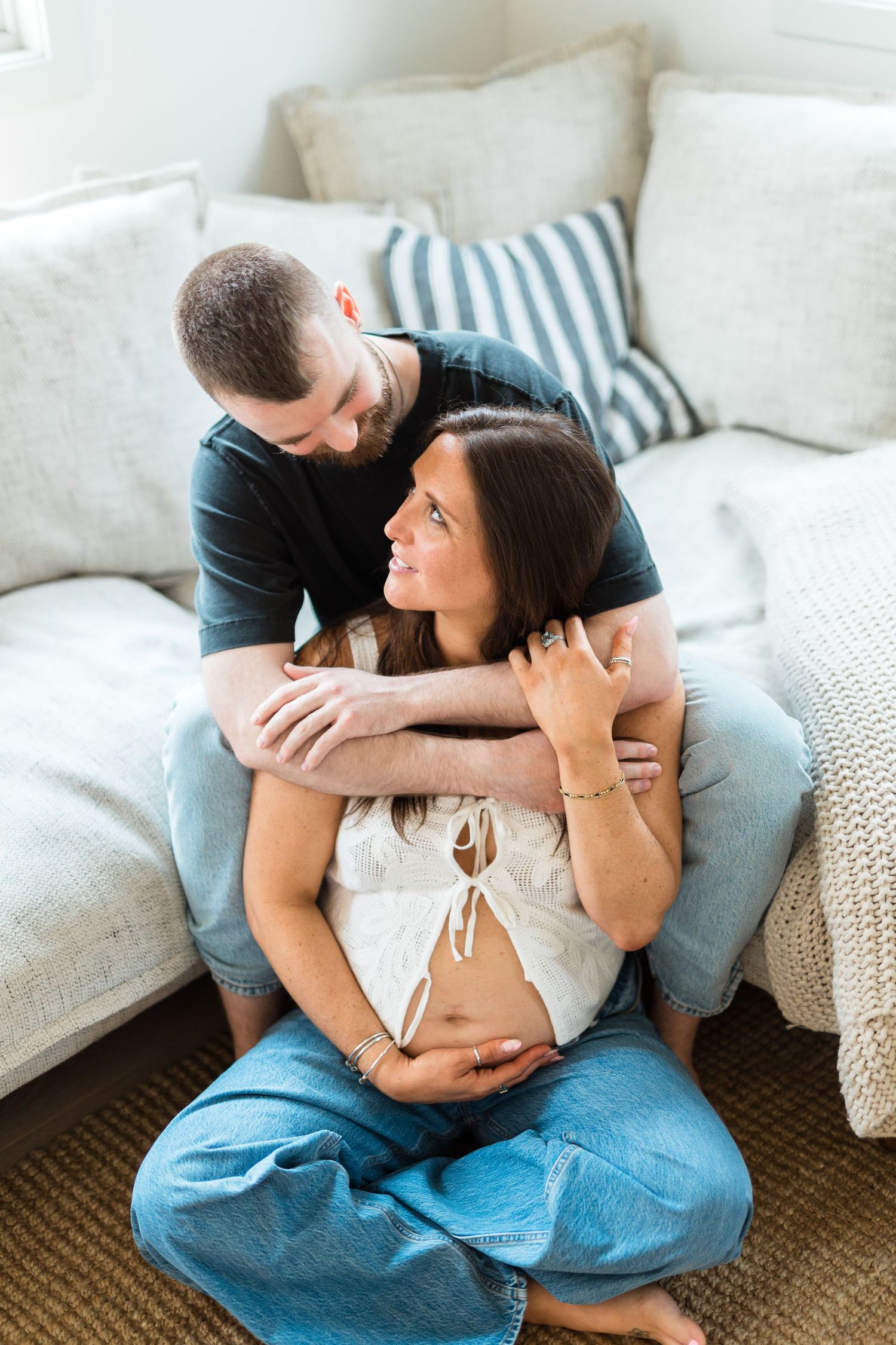 A couple shares an intimate moment on the floor while embracing a pregnant belly in a cozy living room setting.