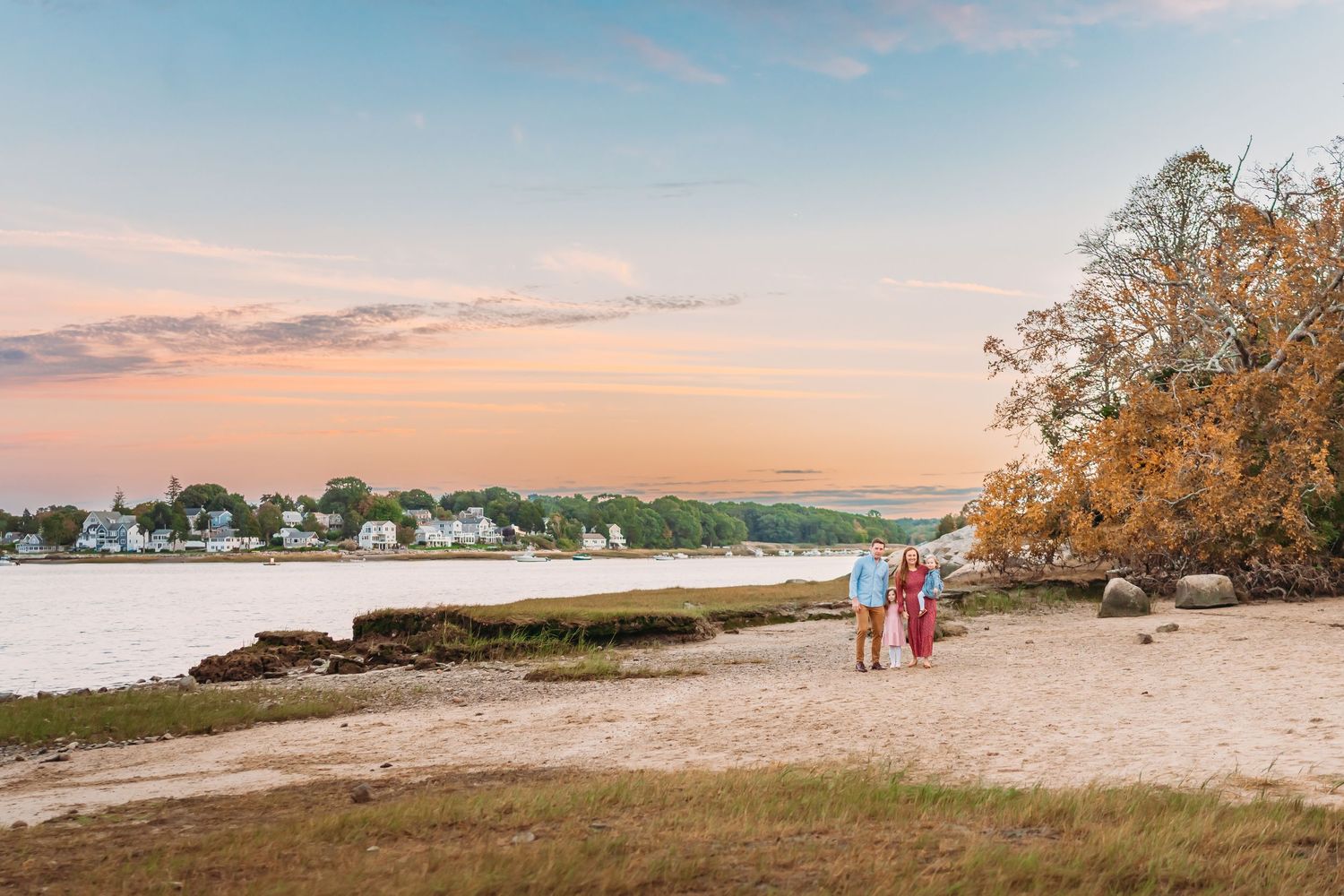 Scenic panoramic view of a beach coastline at sunset with golden clouds and trees along the shore.