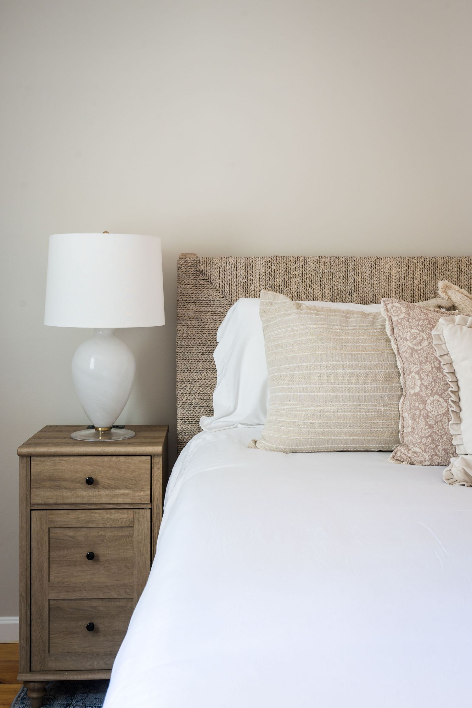 Modern bedroom decor featuring a white bed with textured pillows, wooden nightstand and white ceramic table lamp.