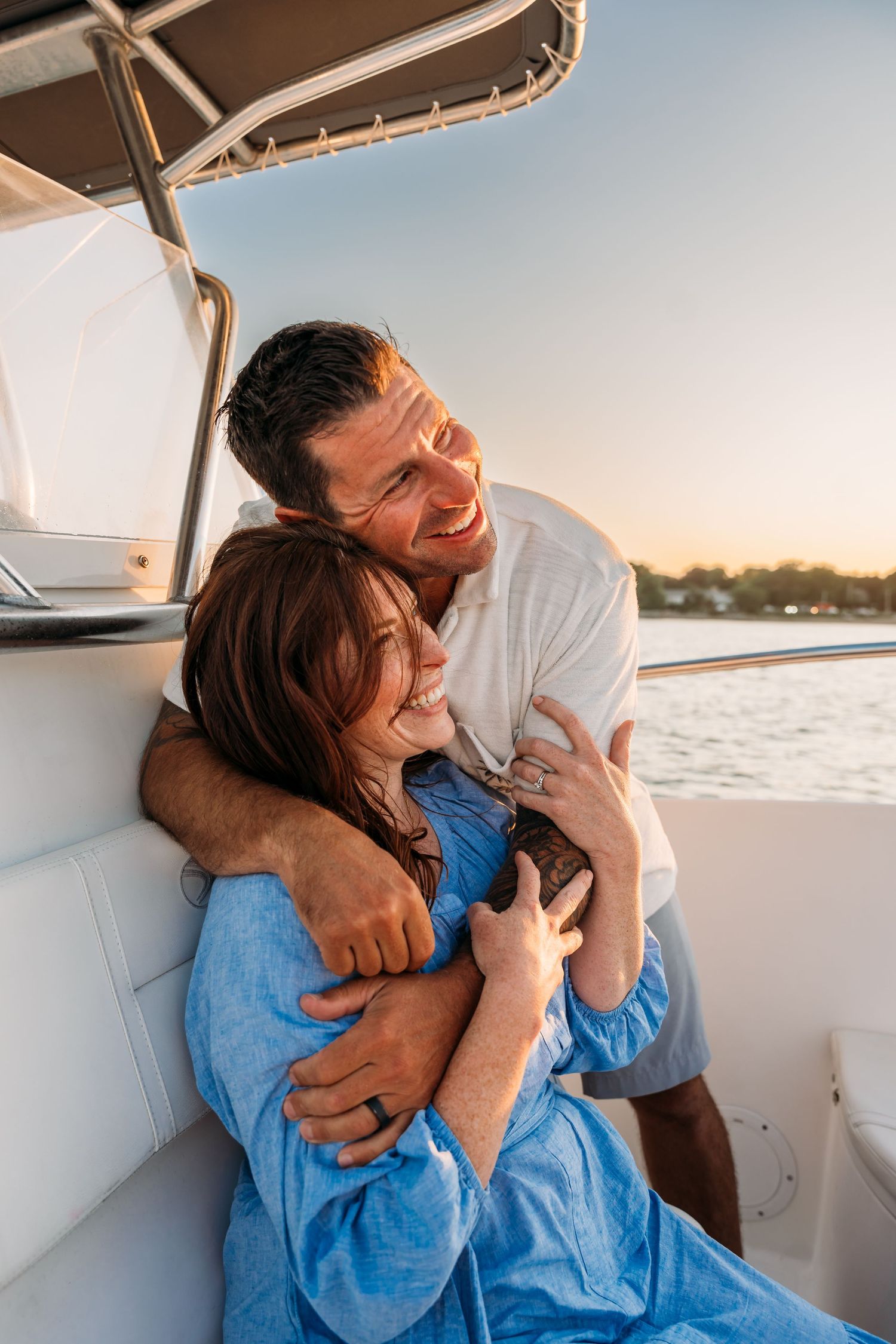 A couple shares joyful laughter while sitting together on a boat during sunset over calm waters.