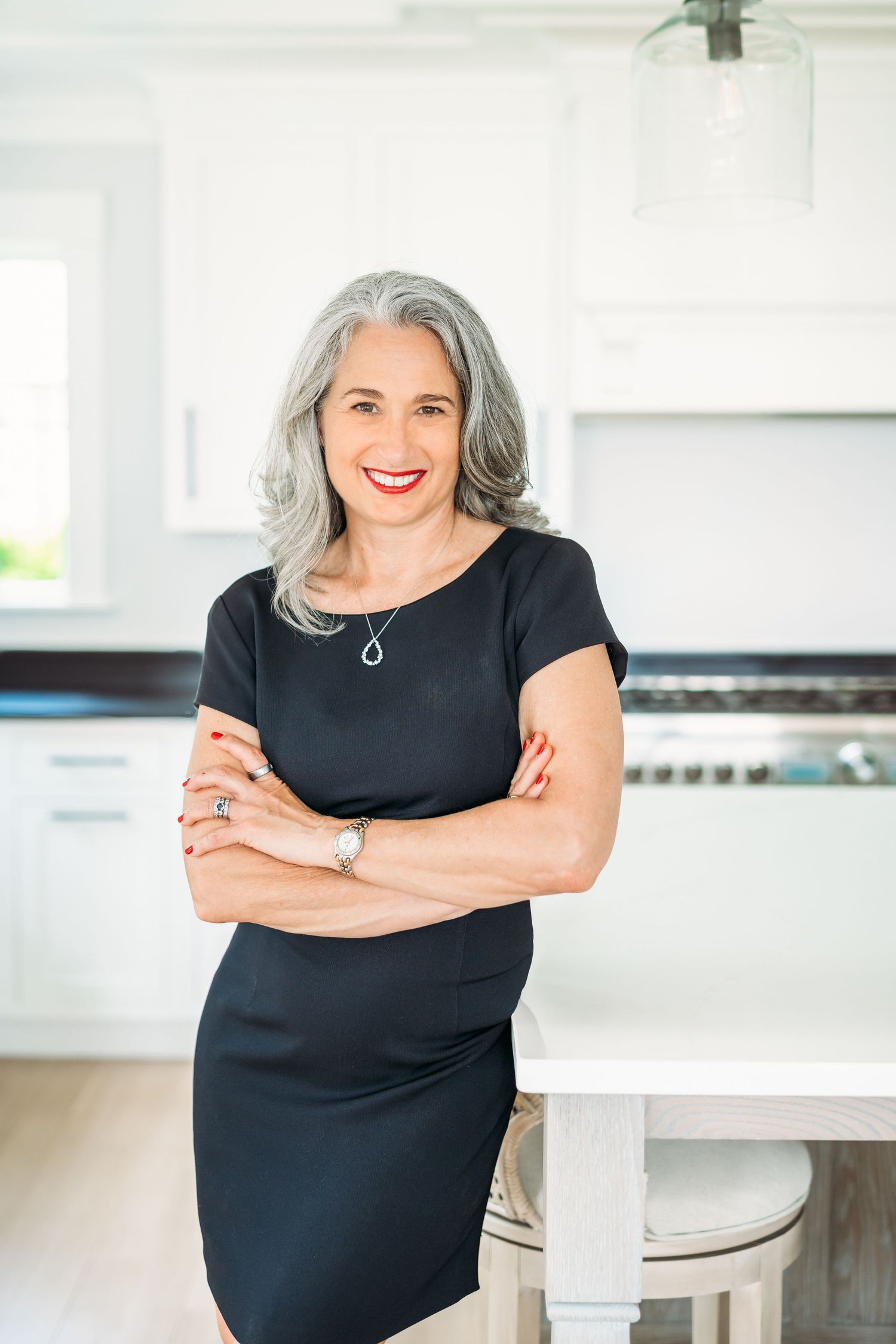 Professional woman in black dress smiles confidently while posing in bright modern kitchen interior.