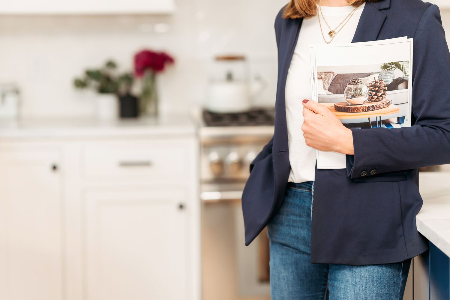 Professional wearing a navy blazer and white top holds a digital tablet while working in a modern office setting.