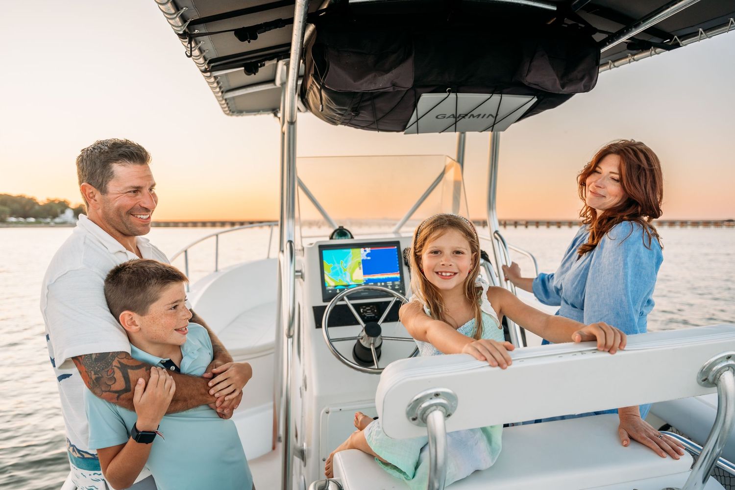 Group of people enjoying a boat ride at sunset while smiling and socializing on a yacht deck.