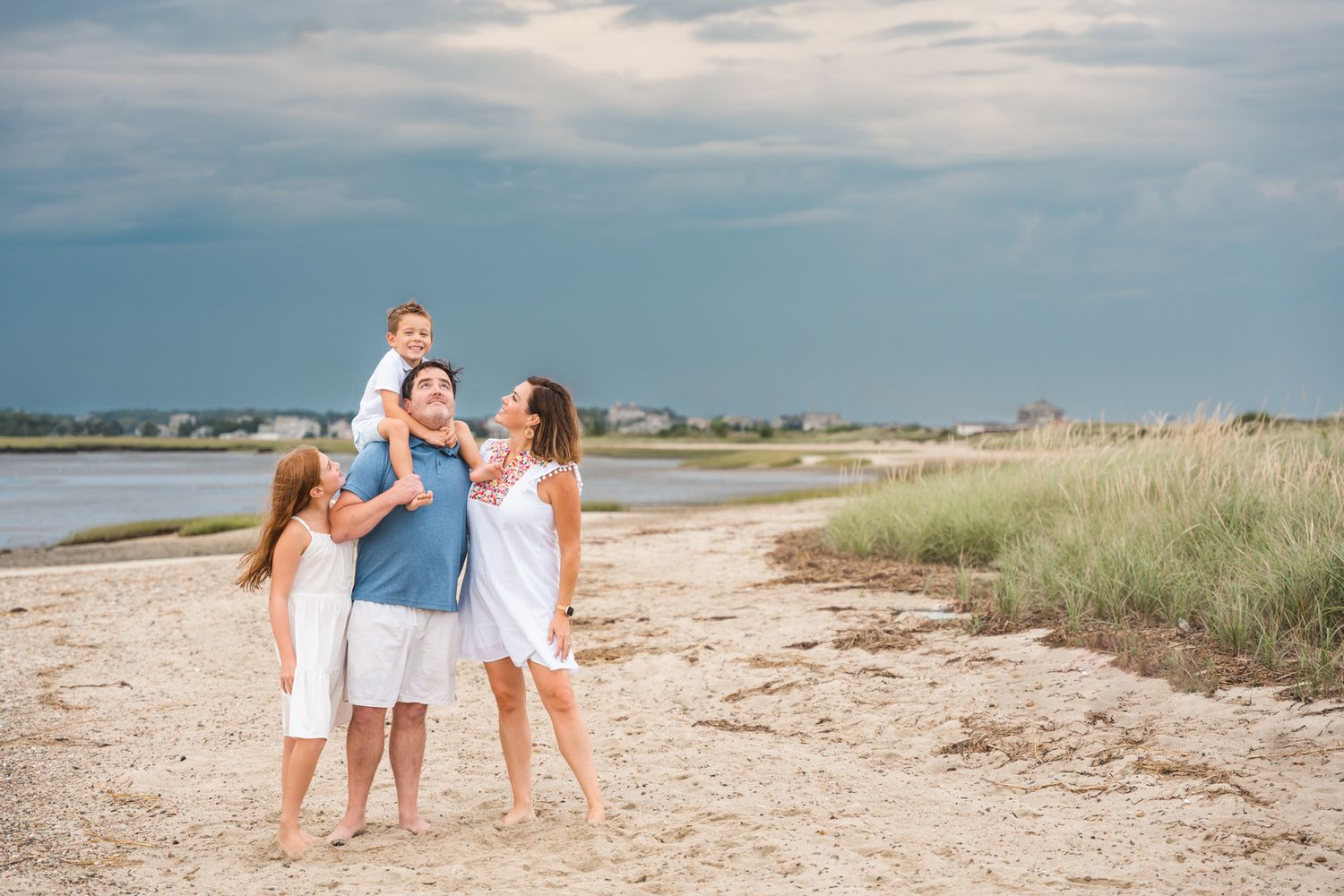 A group enjoying a summer day together on a sandy beach with coastal grass and blue waters in the background.
