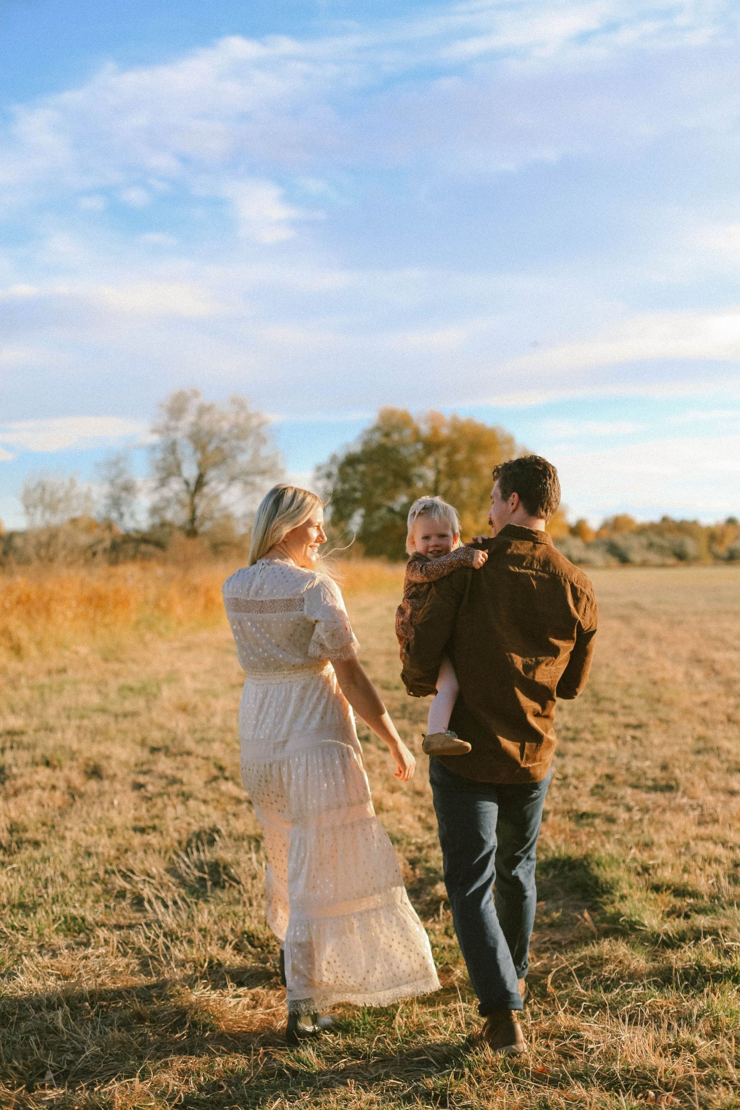 Family walking together in a golden field during sunset.