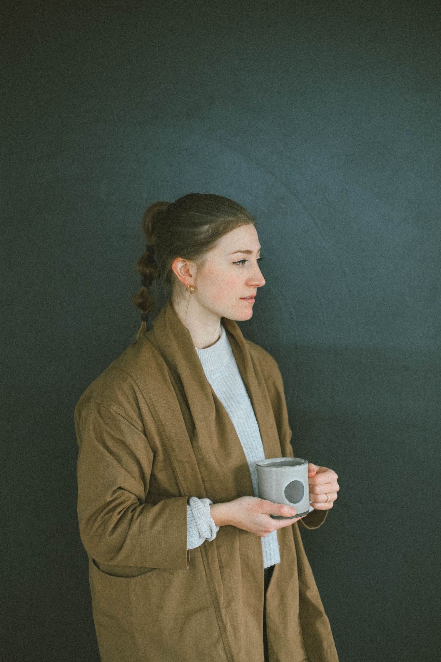 Side view of someone in a brown coat holding a coffee cup against a dark background.