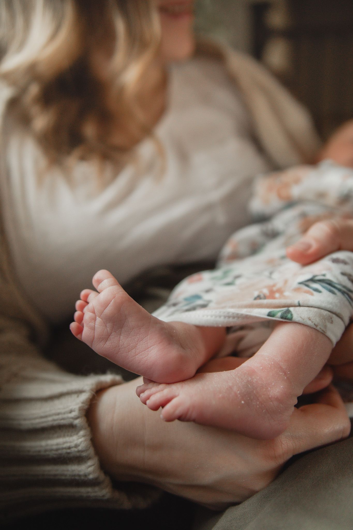 Close-up of tiny newborn baby feet resting in mother's arms, wrapped in a floral blanket.