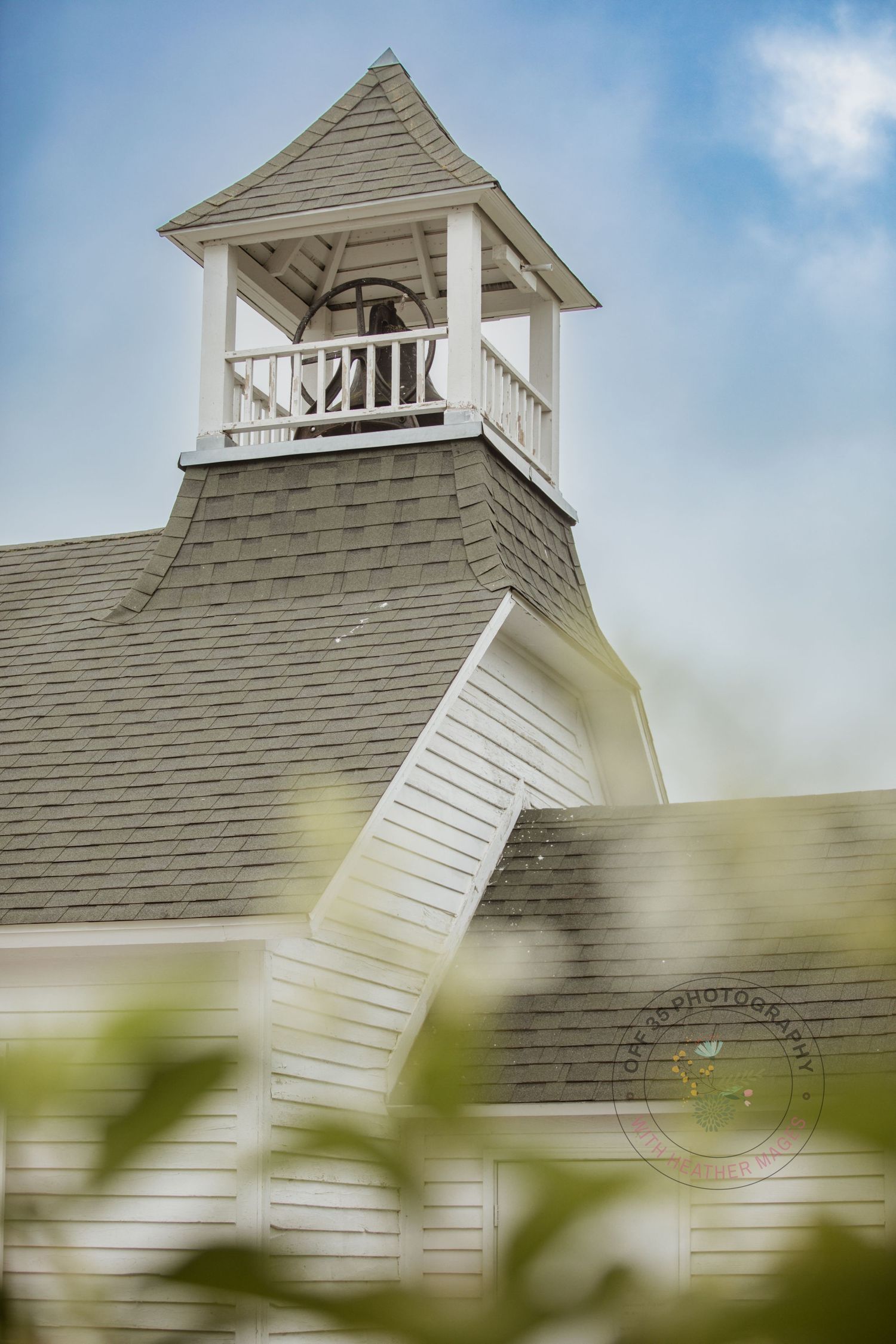 White church steeple with bell tower against blue sky, photographed through soft focus foliage.