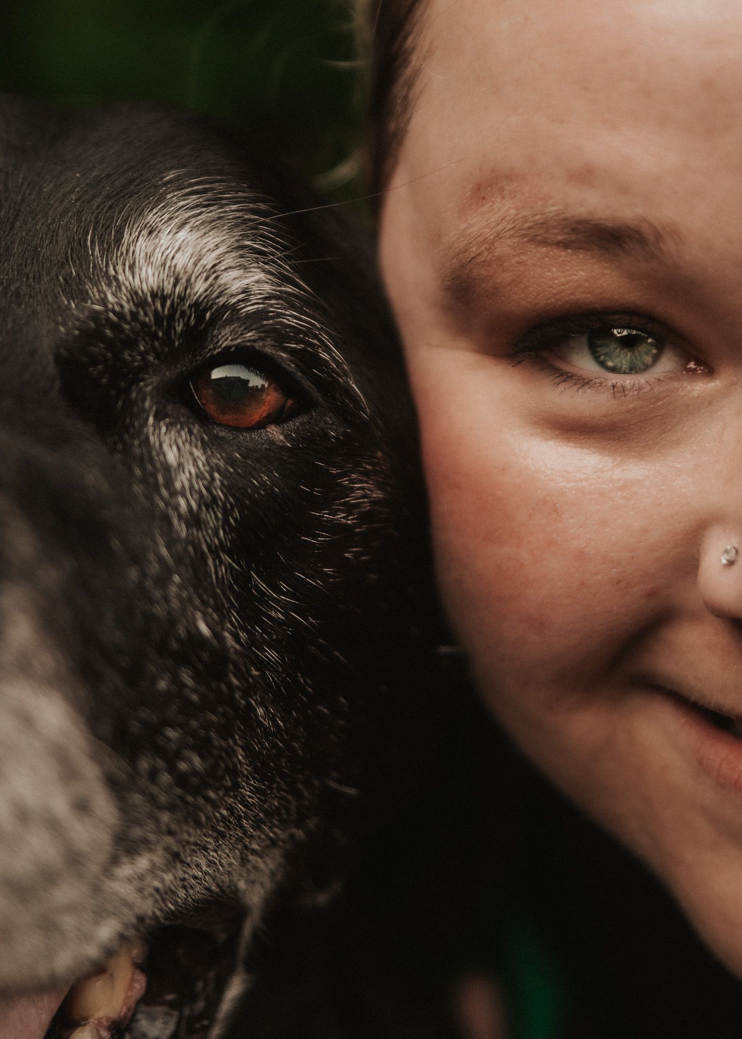 Close-up portrait of a woman and her black dog cheek to cheek, showcasing their bond and matching soulful eyes.