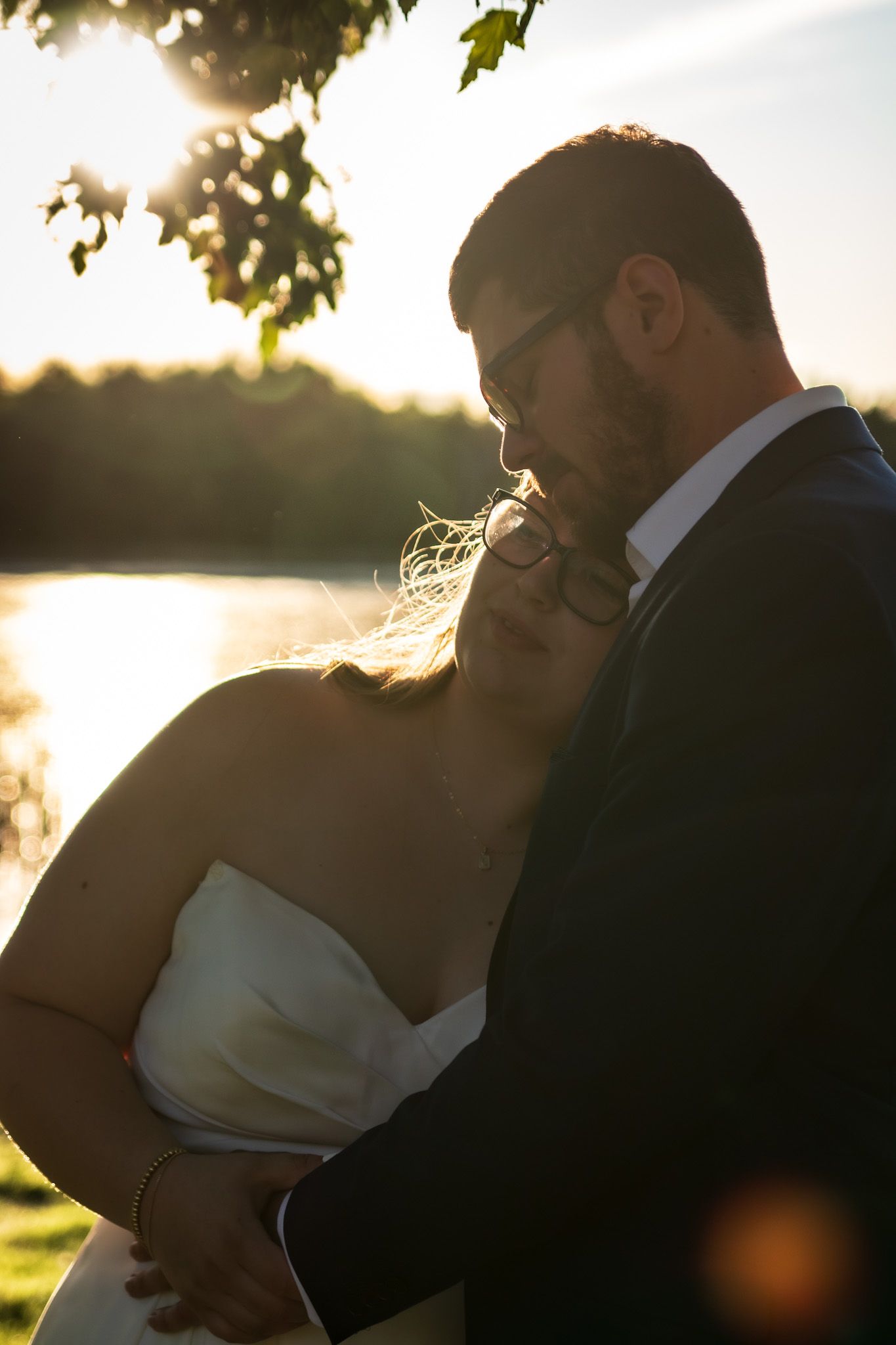A romantic sunset silhouette shows a bride and groom embracing and kissing outdoors under golden sunlight.