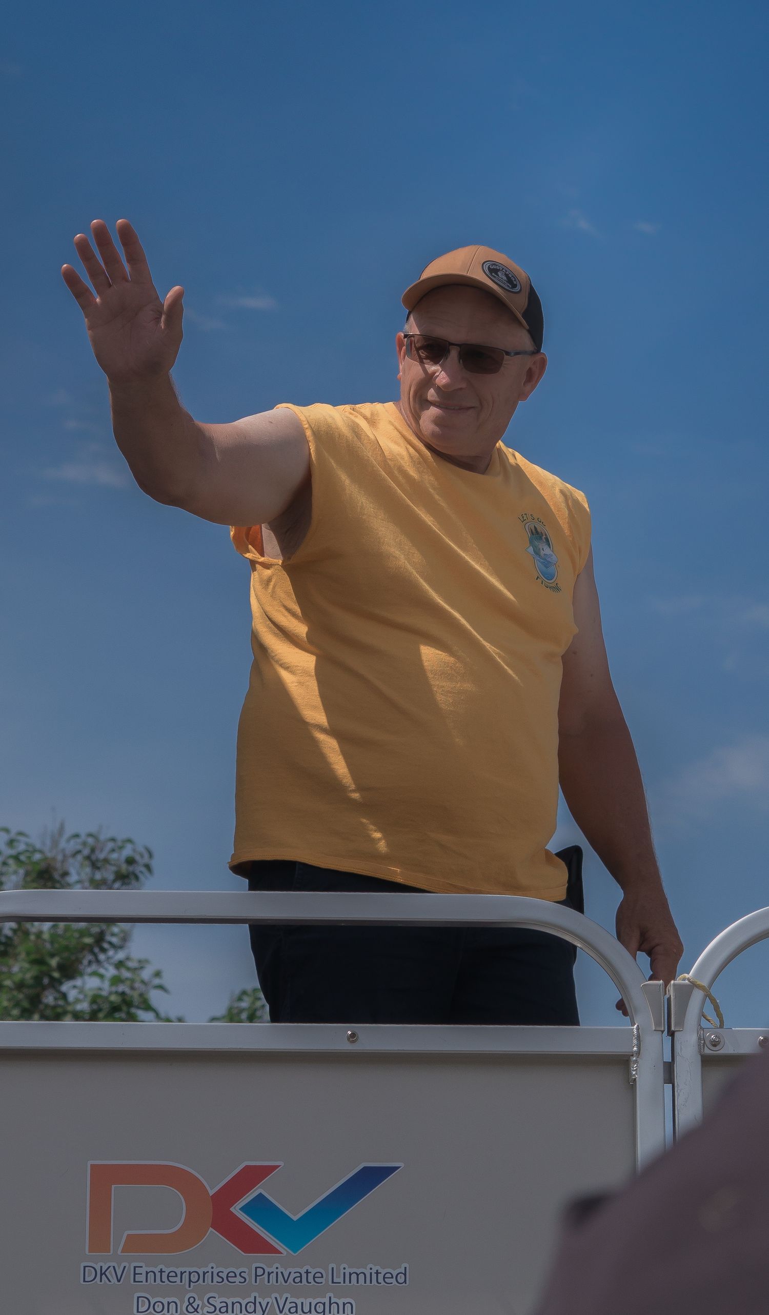 Person in yellow shirt waving from inside a DKV Enterprise vehicle against blue sky background.