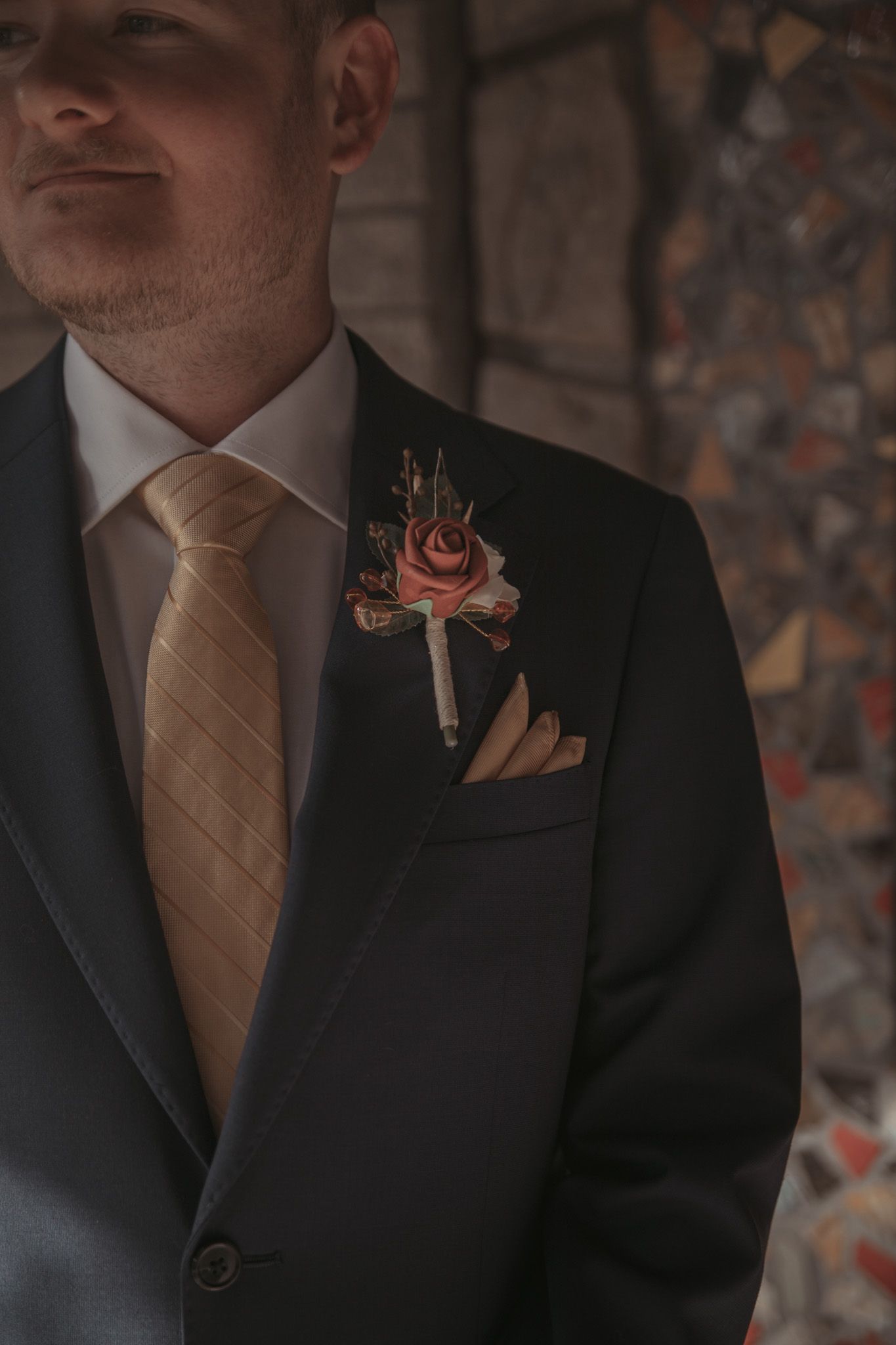 A close-up detail shot showing the torso of a person wearing a black suit jacket with a peach-colored boutonniere.