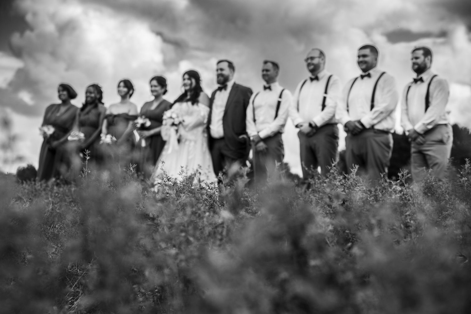 Wedding party in black and white poses together in tall grass against a natural outdoor backdrop.