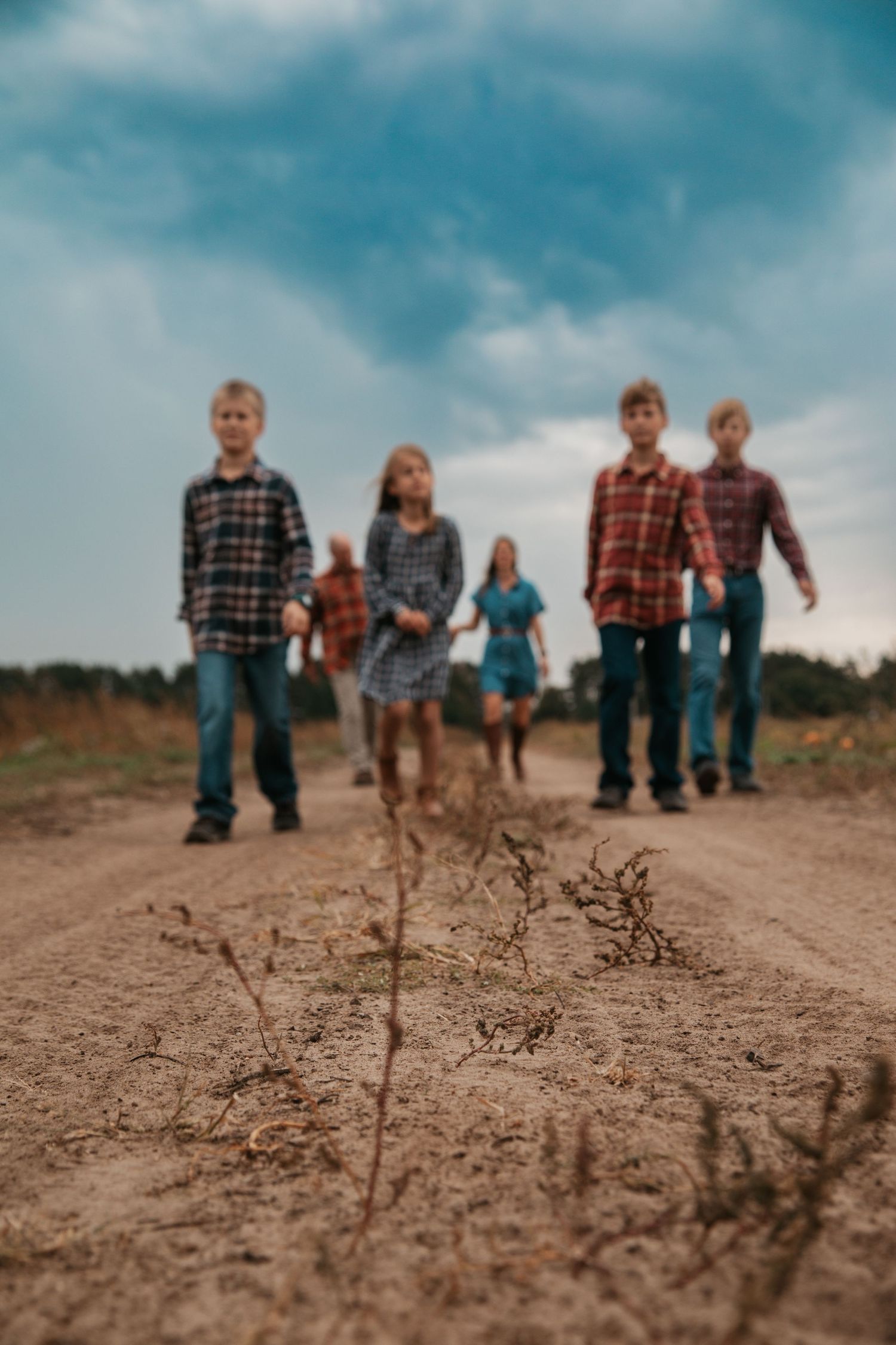 A group walks along a dirt path under blue skies with dried plants in the foreground.
