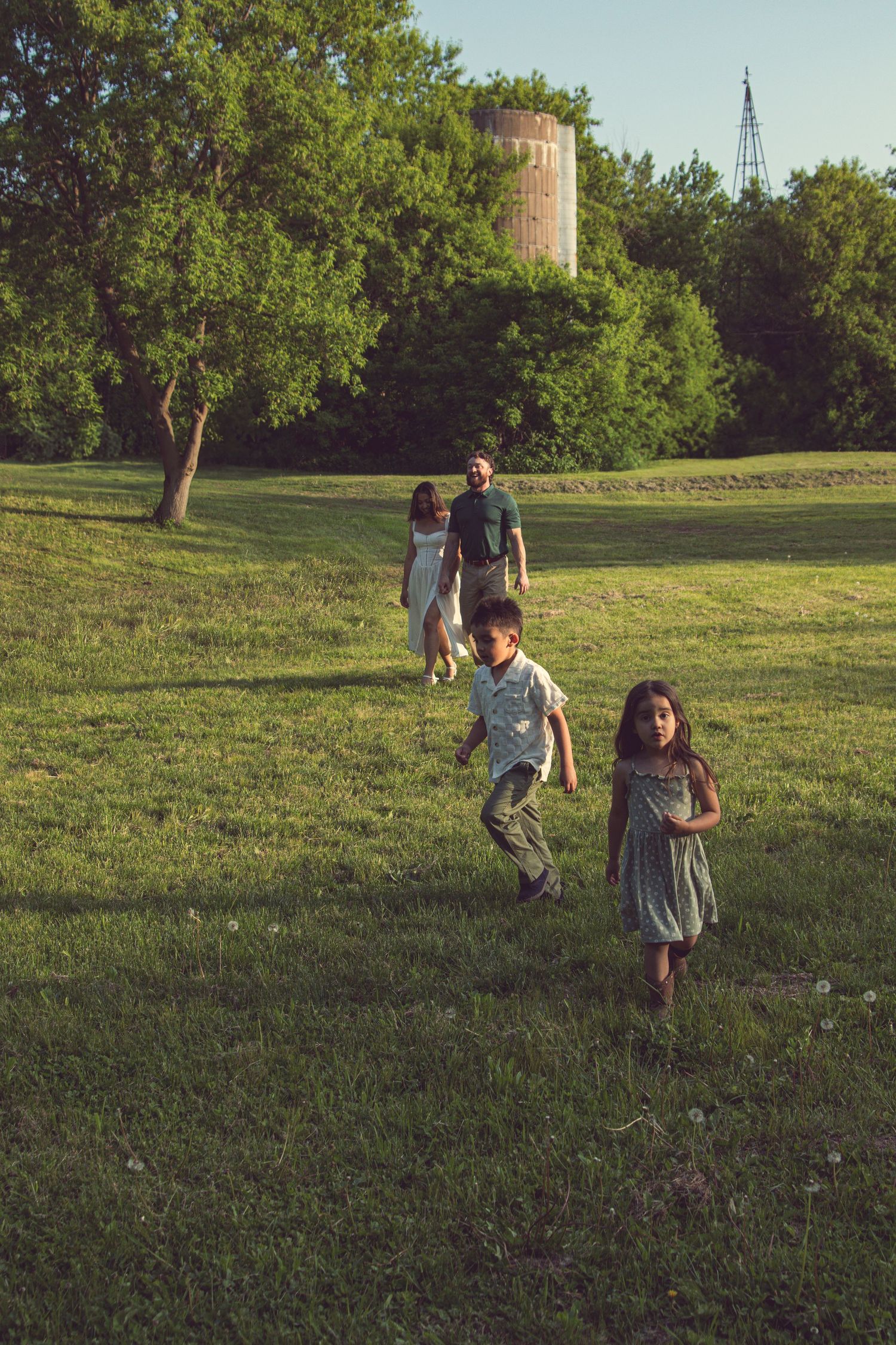 A family plays and runs together on a grassy hillside during golden hour in a park setting.