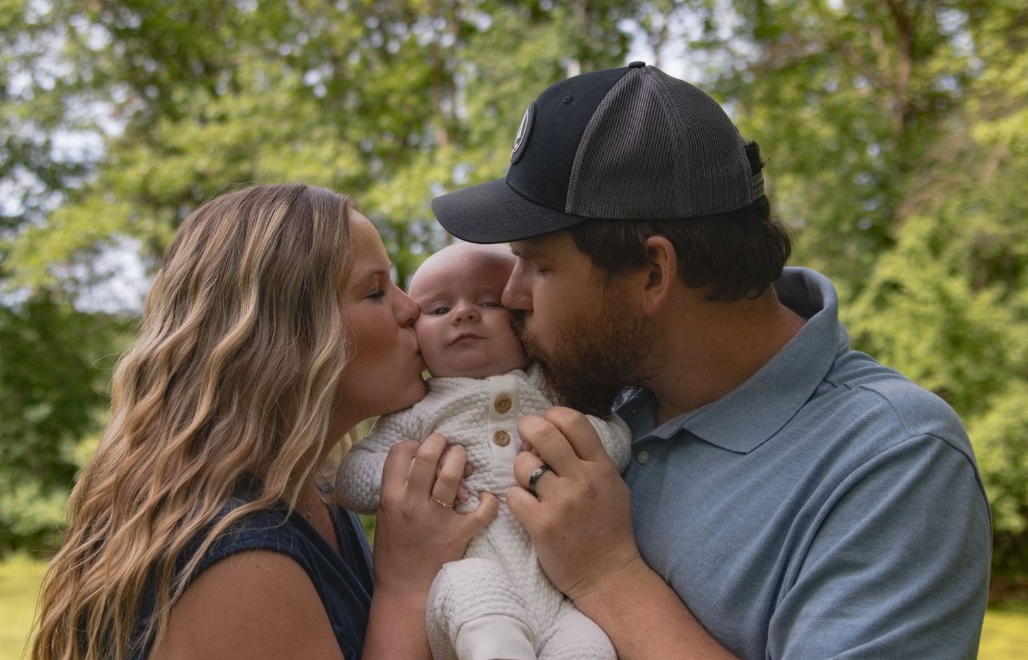 Parents sharing a loving moment with their infant baby outdoors on a sunny day.
