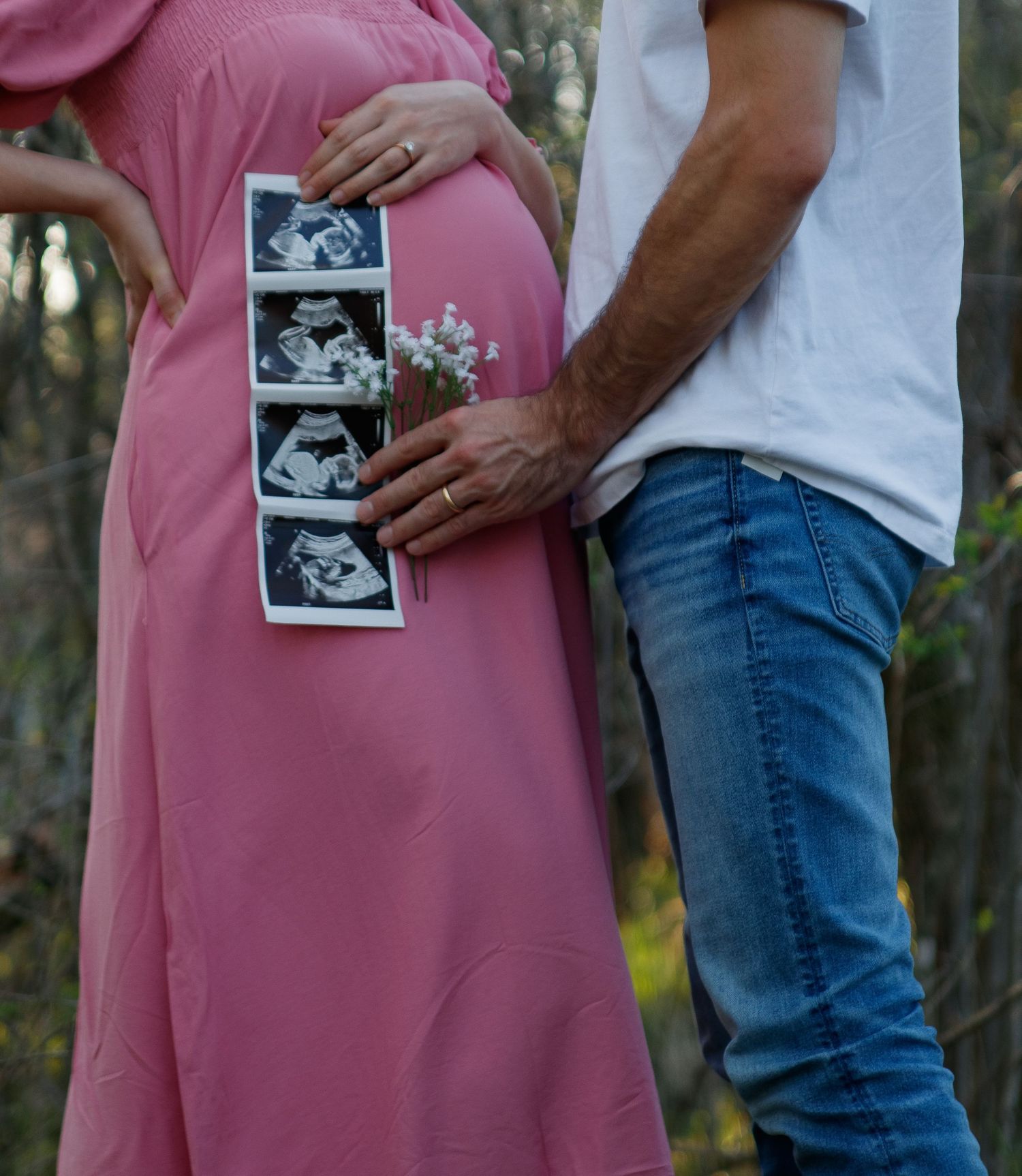 A couple holds ultrasound photos while embracing in a pregnancy announcement photoshoot outdoors.