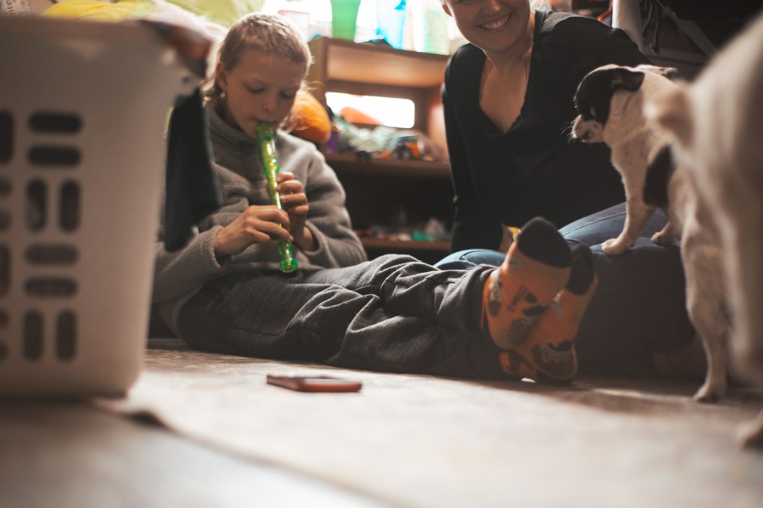Family relaxing on floor with kids playing, woman smiling, and a dog joining the fun in a cozy home.