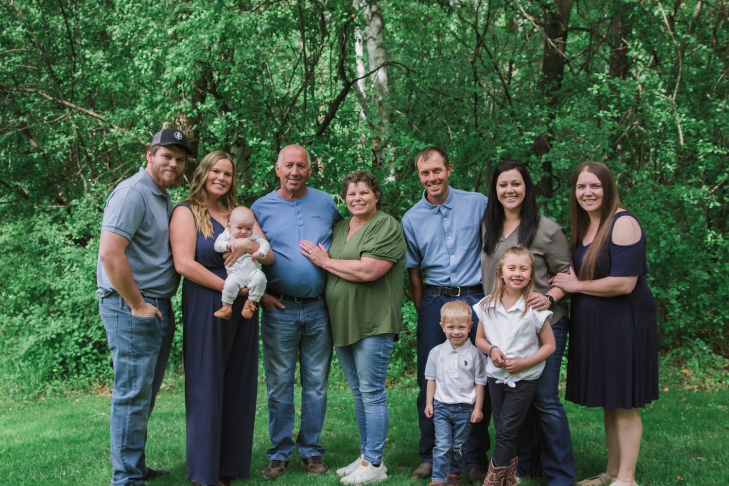 A group photo session in a lush green outdoor setting with people arranged in casual poses.