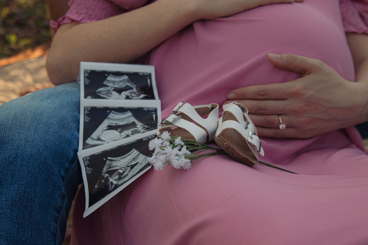 A series of ultrasound photos being held over a pink fabric surface showing the progression of a pregnancy.